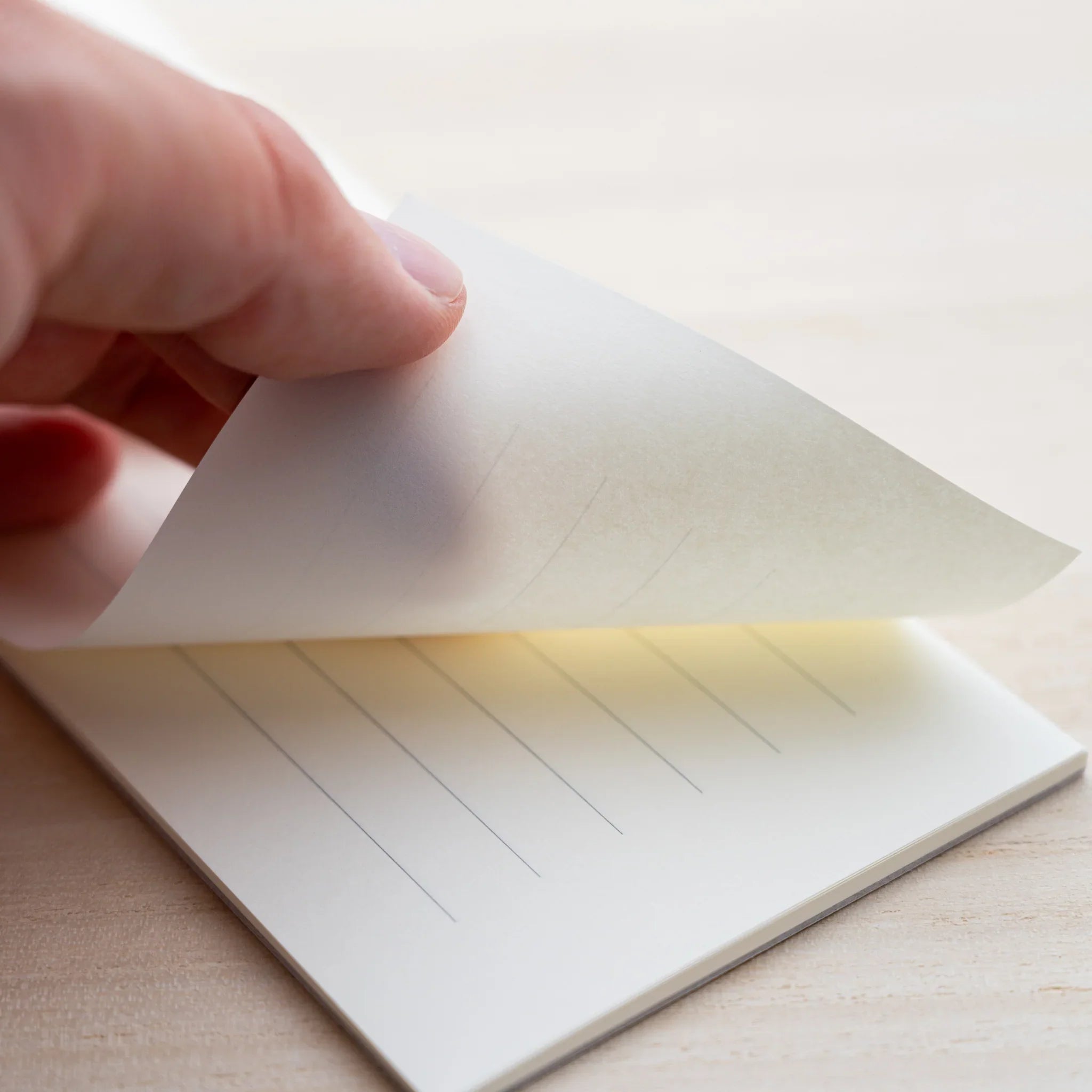 Hand lifting a sheet of MD Paper letter pad showing cream paper with vertical ruled lines