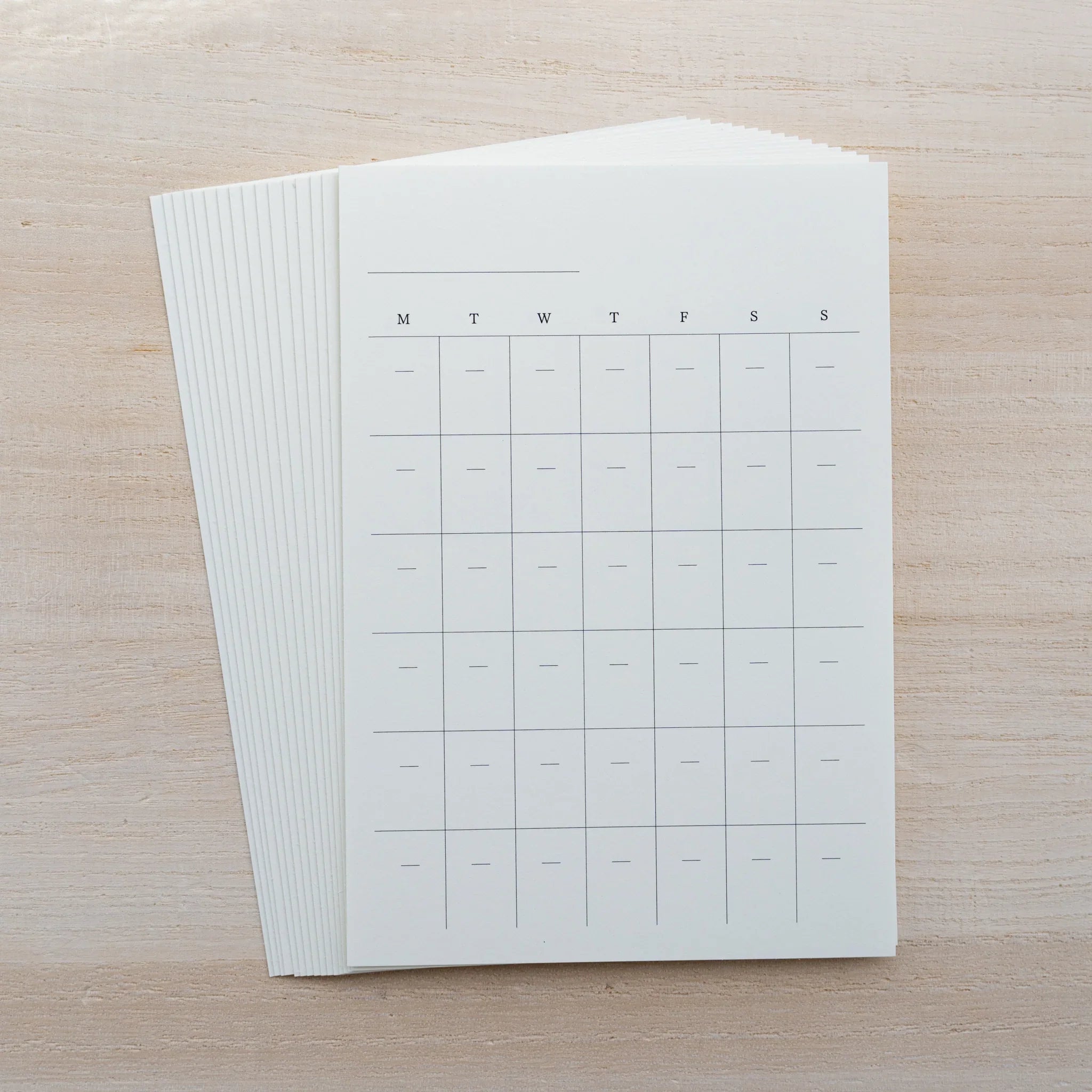 Stack of MD Diary Sticker sheets showing a monthly calendar grid with M T W T F S S columns, fanned on wood