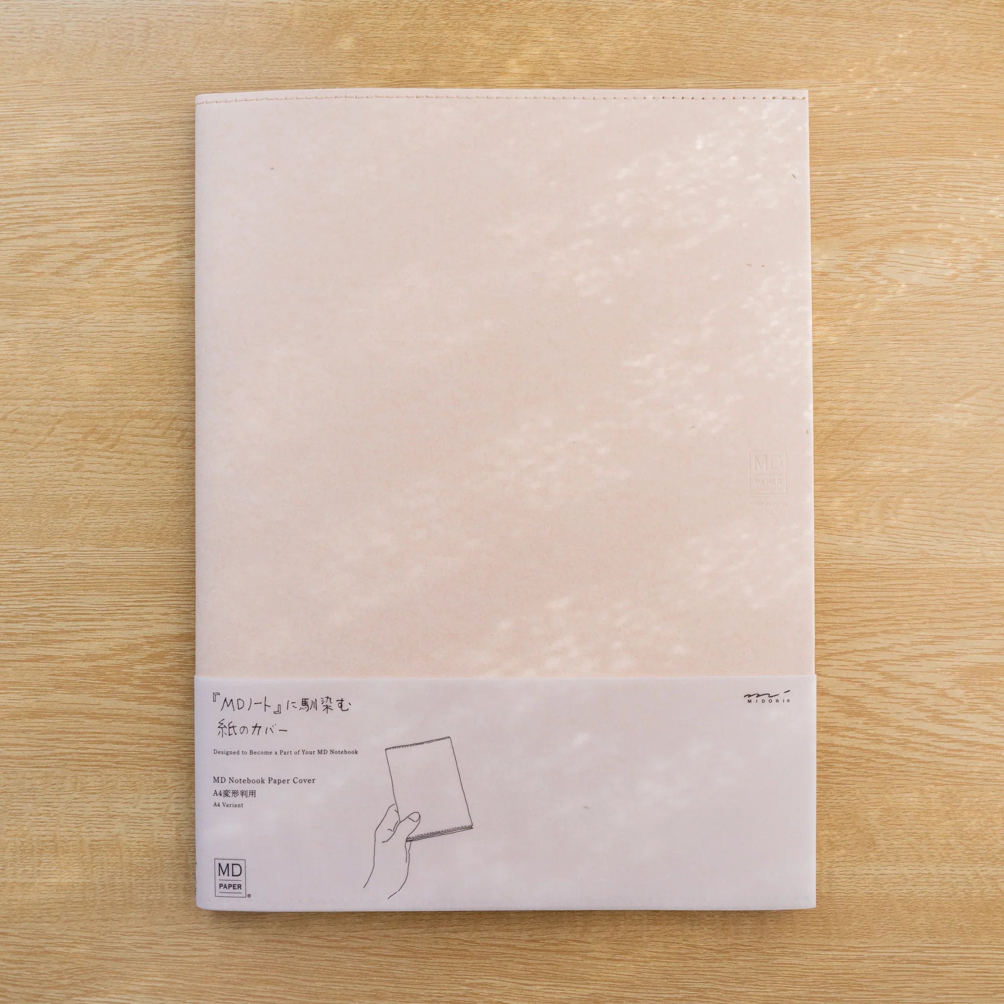MD Notebook Paper Cover A4 Variant in pale pink Cordoba paper with belly band, front view on wood