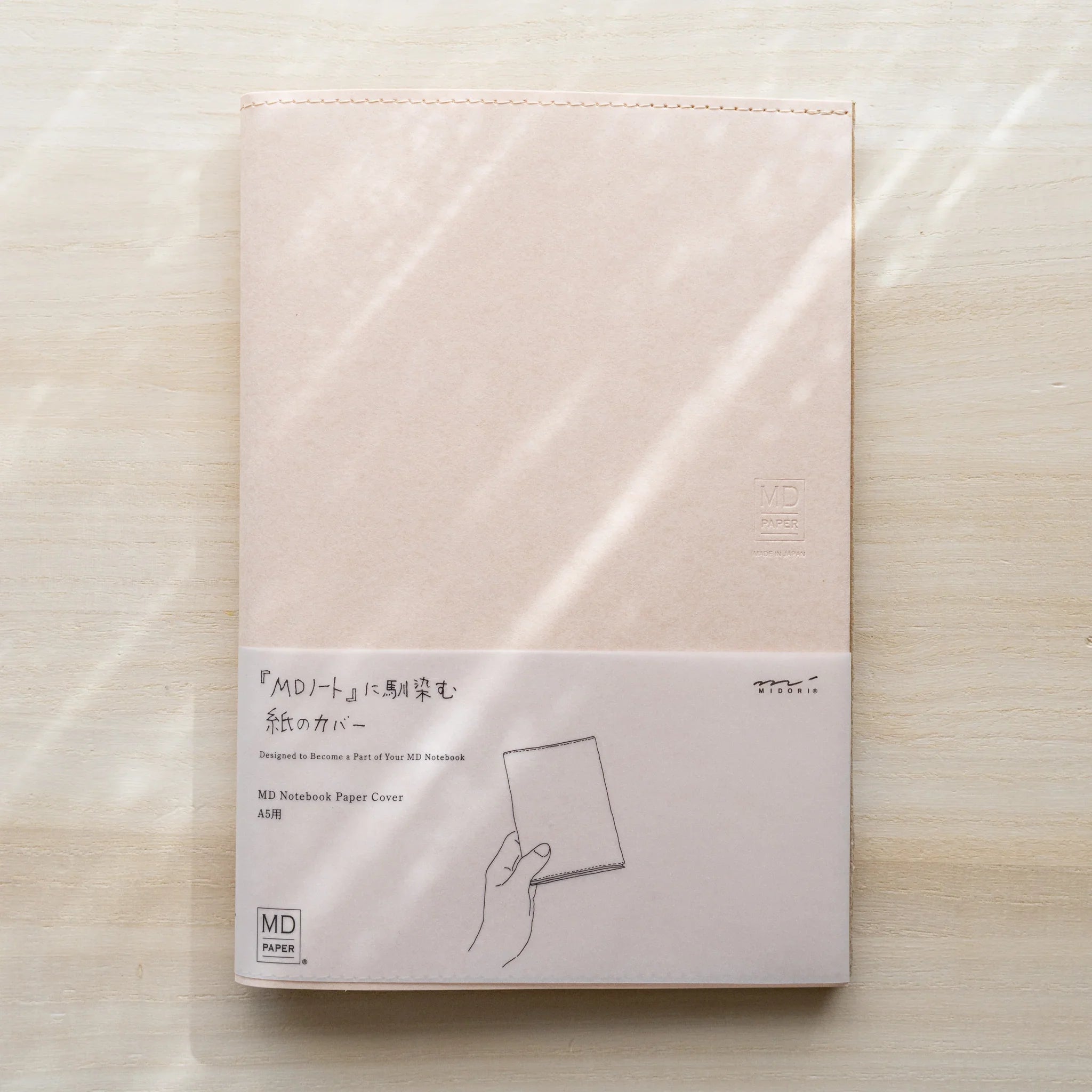 Midori MD Notebook Paper Cover A5, pale paper, belly band with hand illustration and MD Paper logo on wood surface