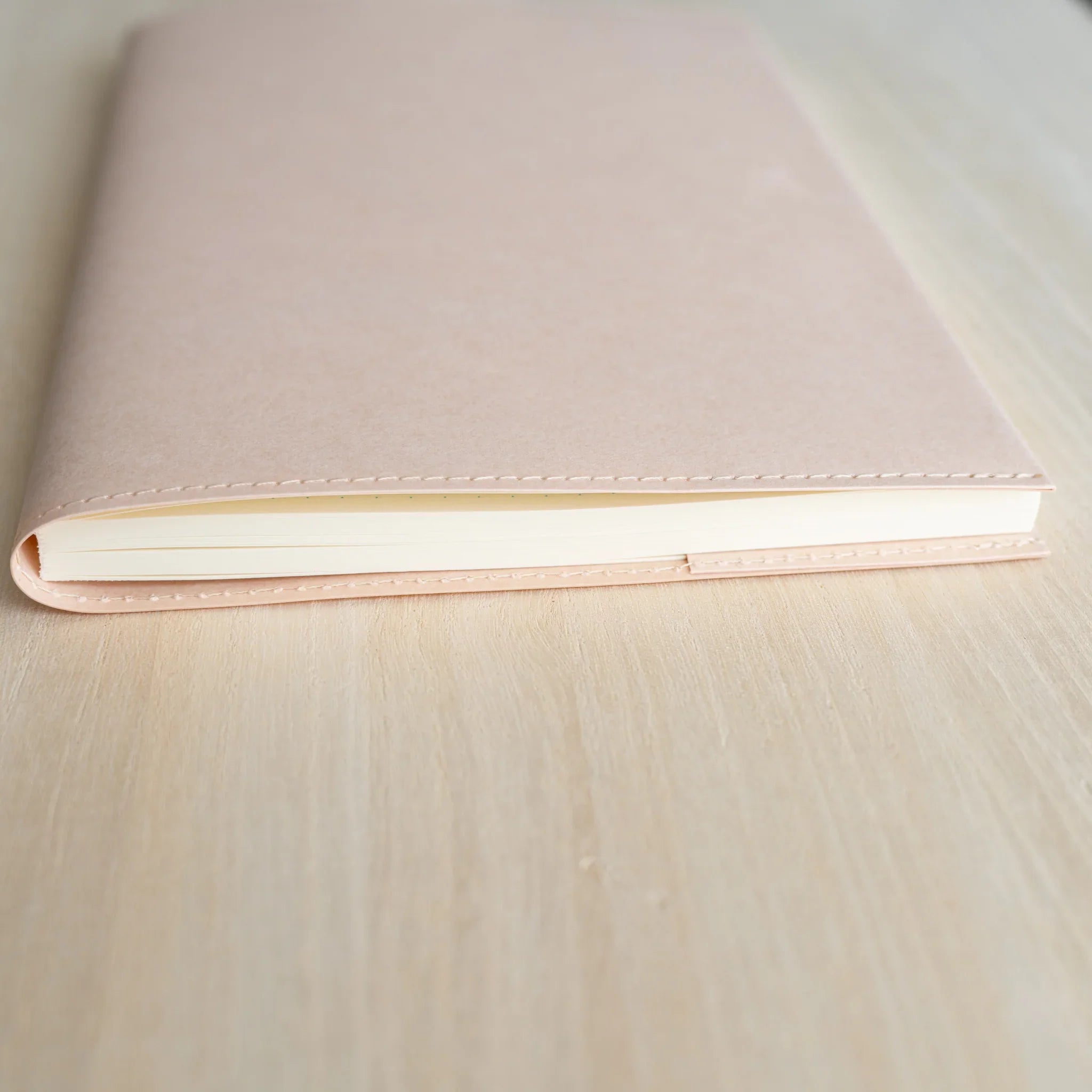 Midori MD Notebook Paper Cover side view showing pale pink paper cover, stitched bottom edge, and ivory notebook page stack