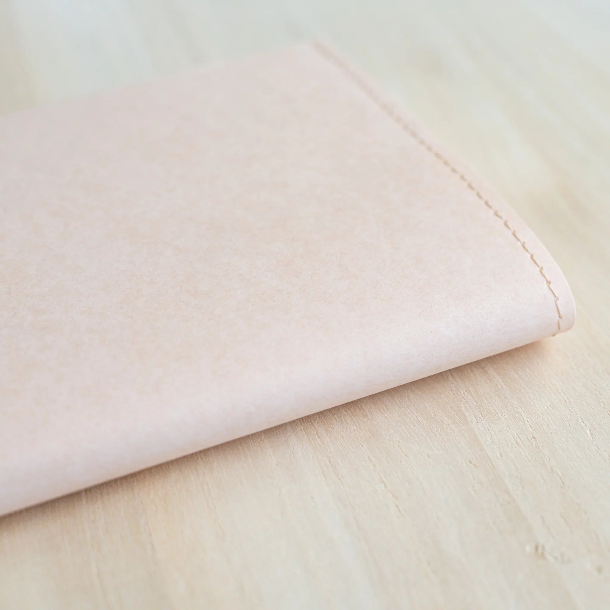 Close-up of MD Paper Notebook Cover top-right corner showing pale paper texture and stitched edge detail on wooden surface