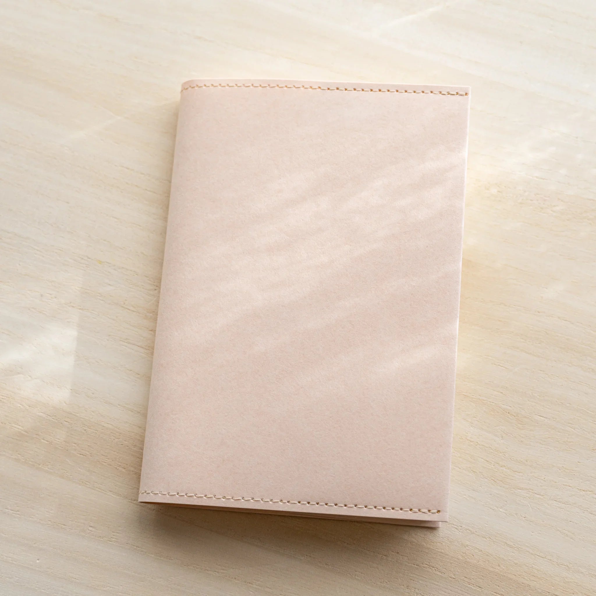 Pale pink MD Notebook Paper Cover, closed front view on a wood surface
