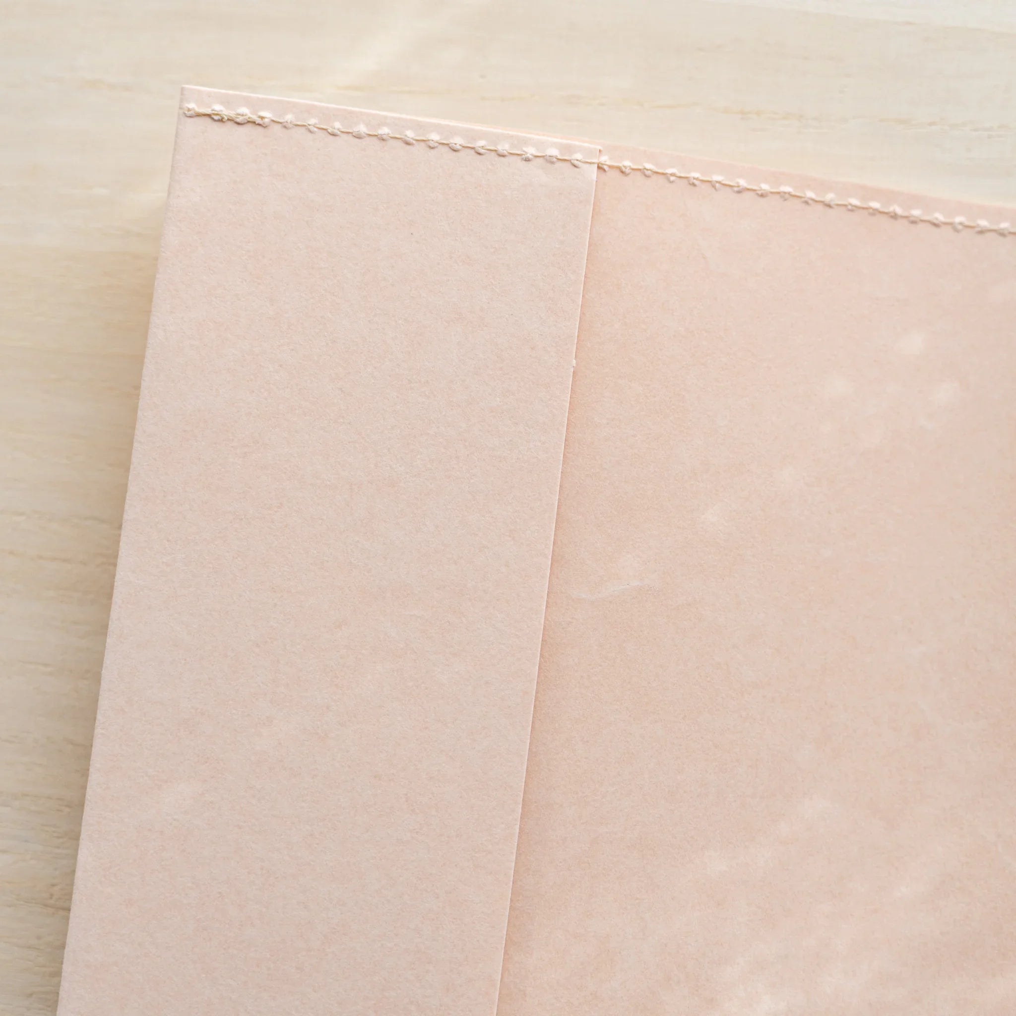 Folded pale pink MD Notebook Paper Cover, angled view on a wood surface