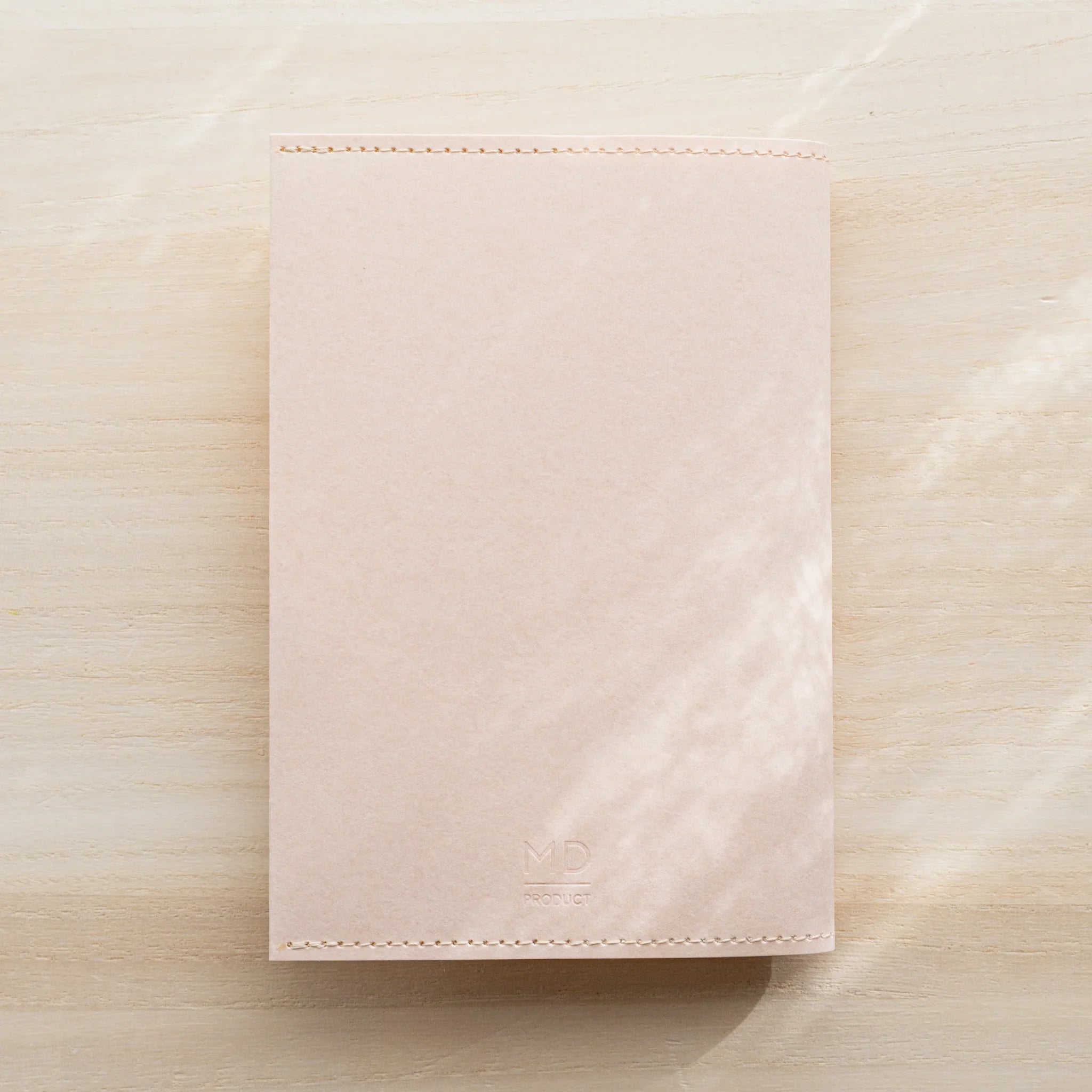 Pale pink MD Notebook Paper Cover, closed front flat lay on a wood surface