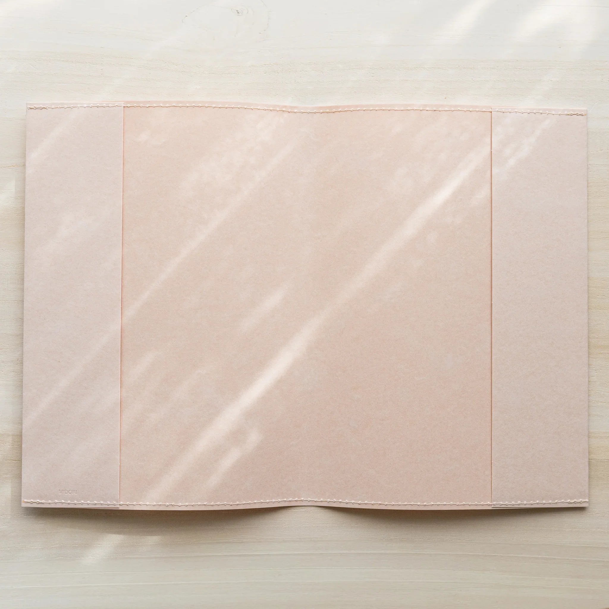 Midori MD Notebook Paper Cover opened flat from above, showing pale paper interior with center spine fold and stitched edges