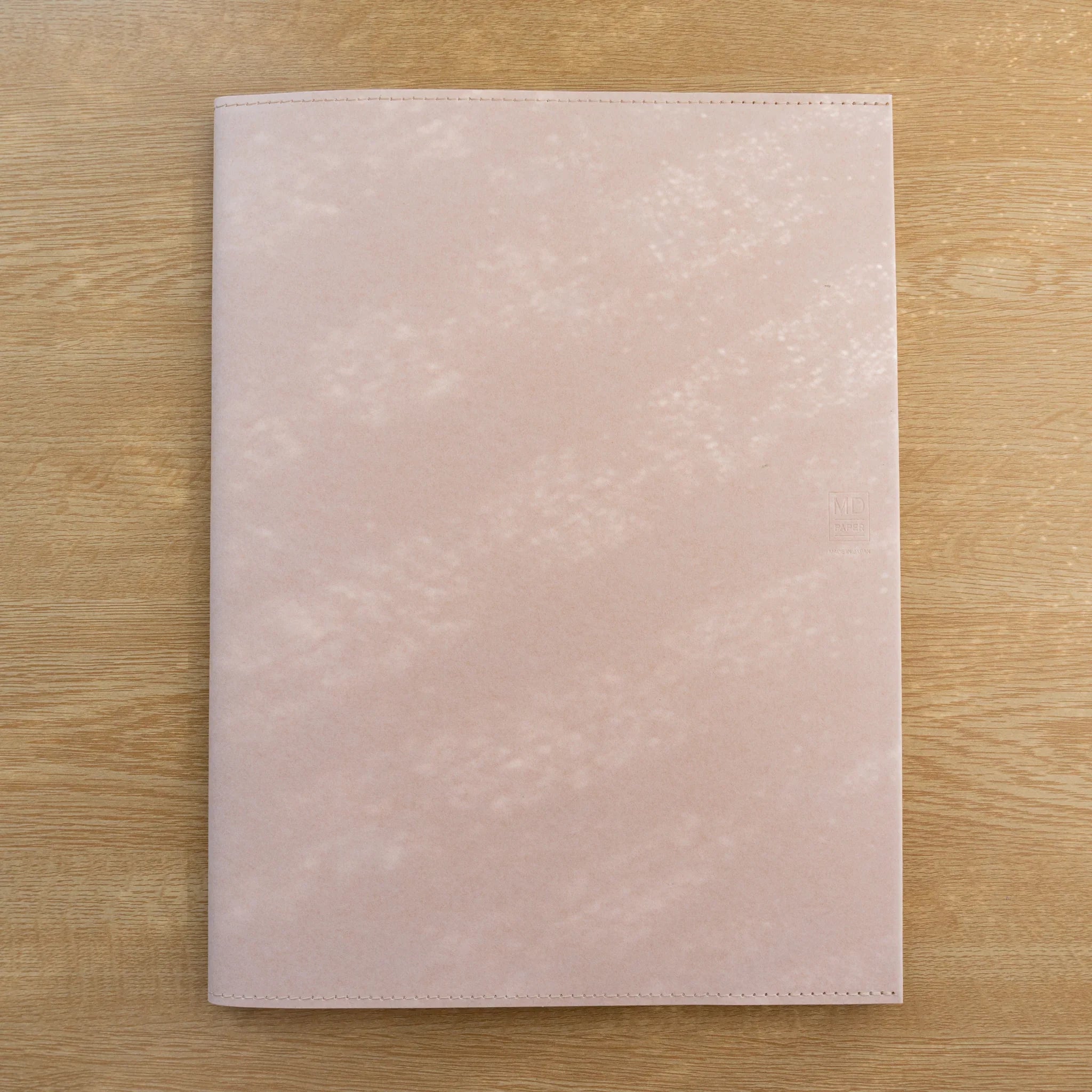 Pale pink MD Notebook Paper Cover, closed front view on a wood surface