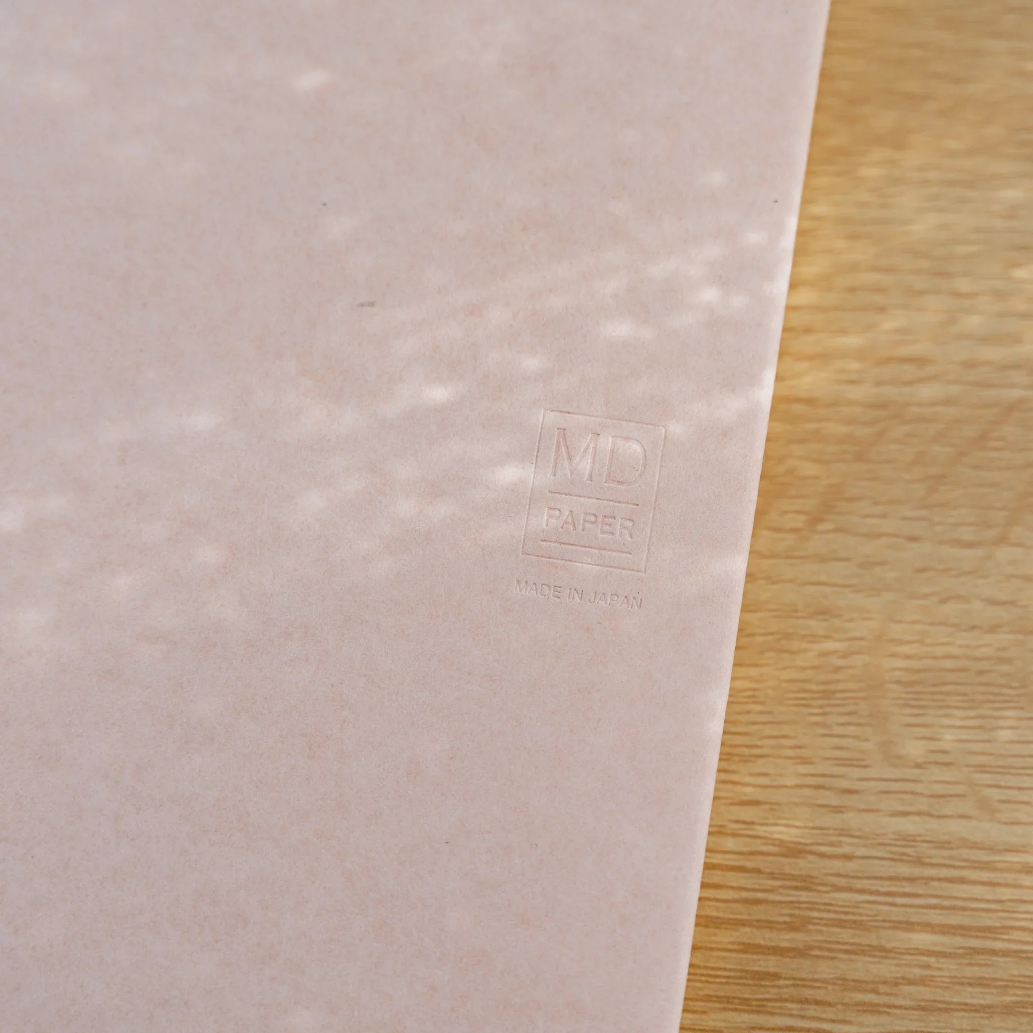 Angled view of a pale pink MD Notebook Paper Cover on a wood surface