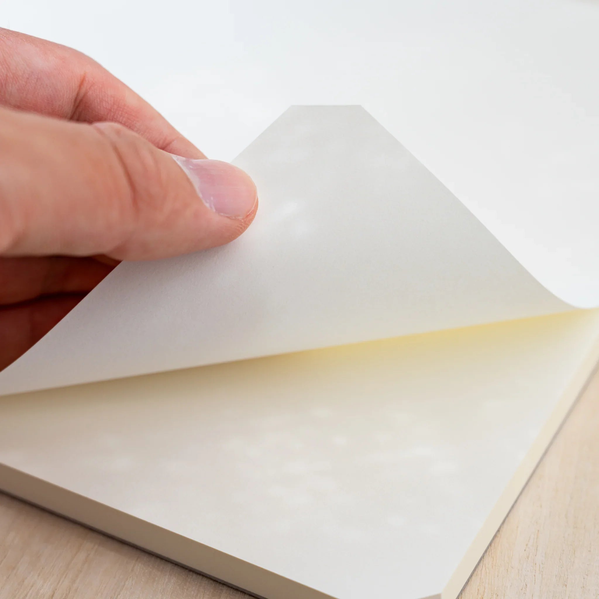 A hand lifting the blank cream top sheet of a Midori MD Paper Pad A4, cut corner visible