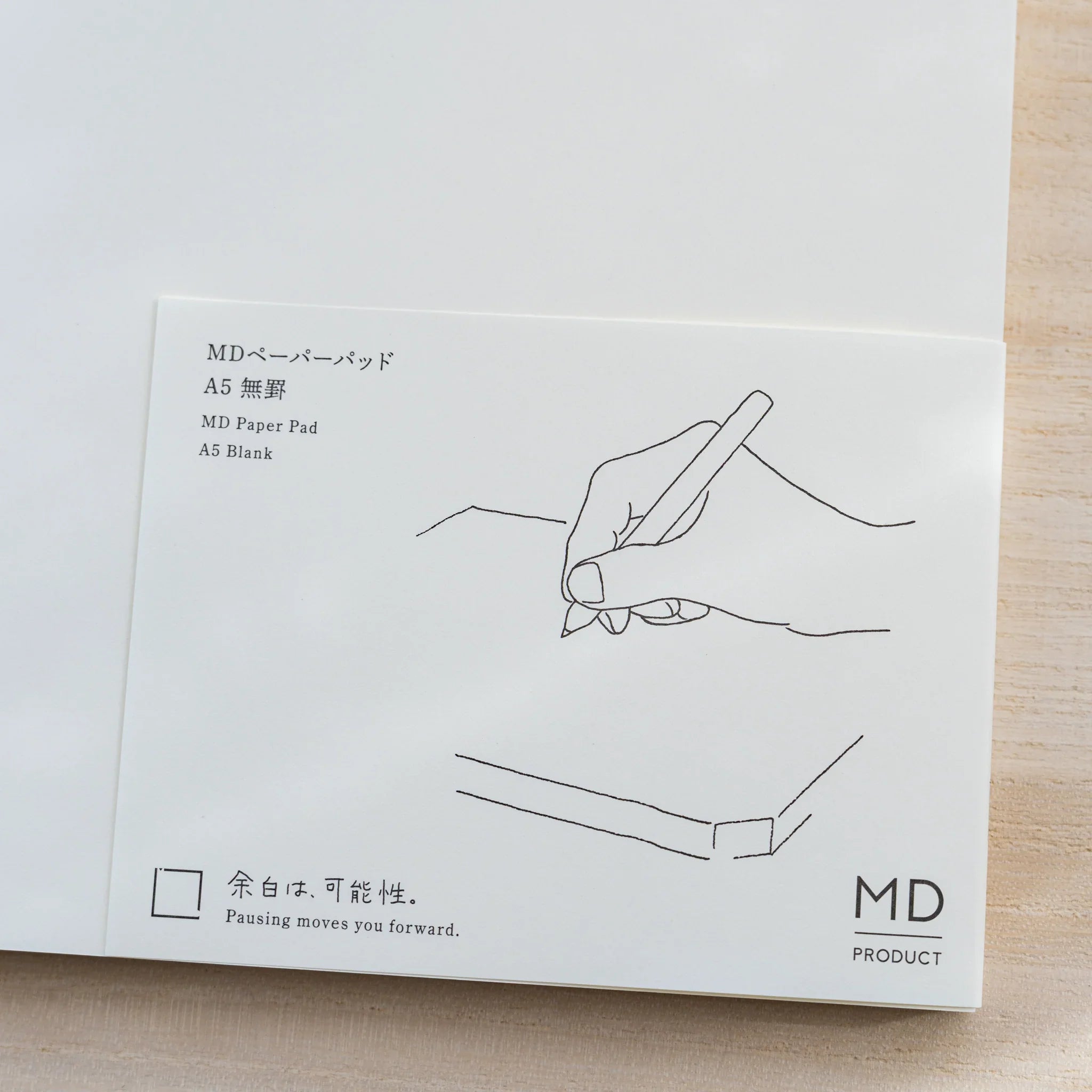 Close-up of Midori MD Paper Pad A5 paper belly band, line drawing of a hand writing and text MD Paper Pad A5 Blank