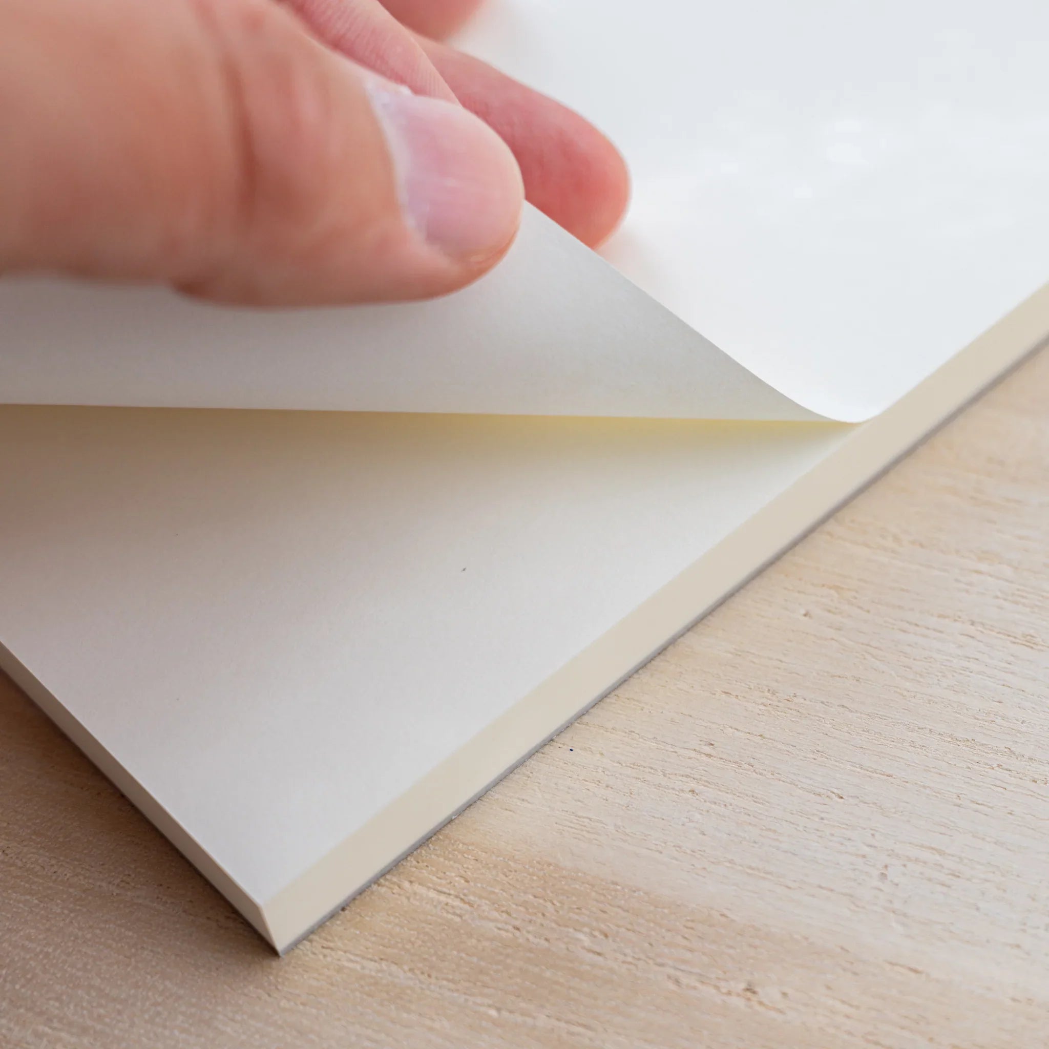 A hand peeling a blank cream sheet from the glued top edge of a Midori MD Paper Pad A5