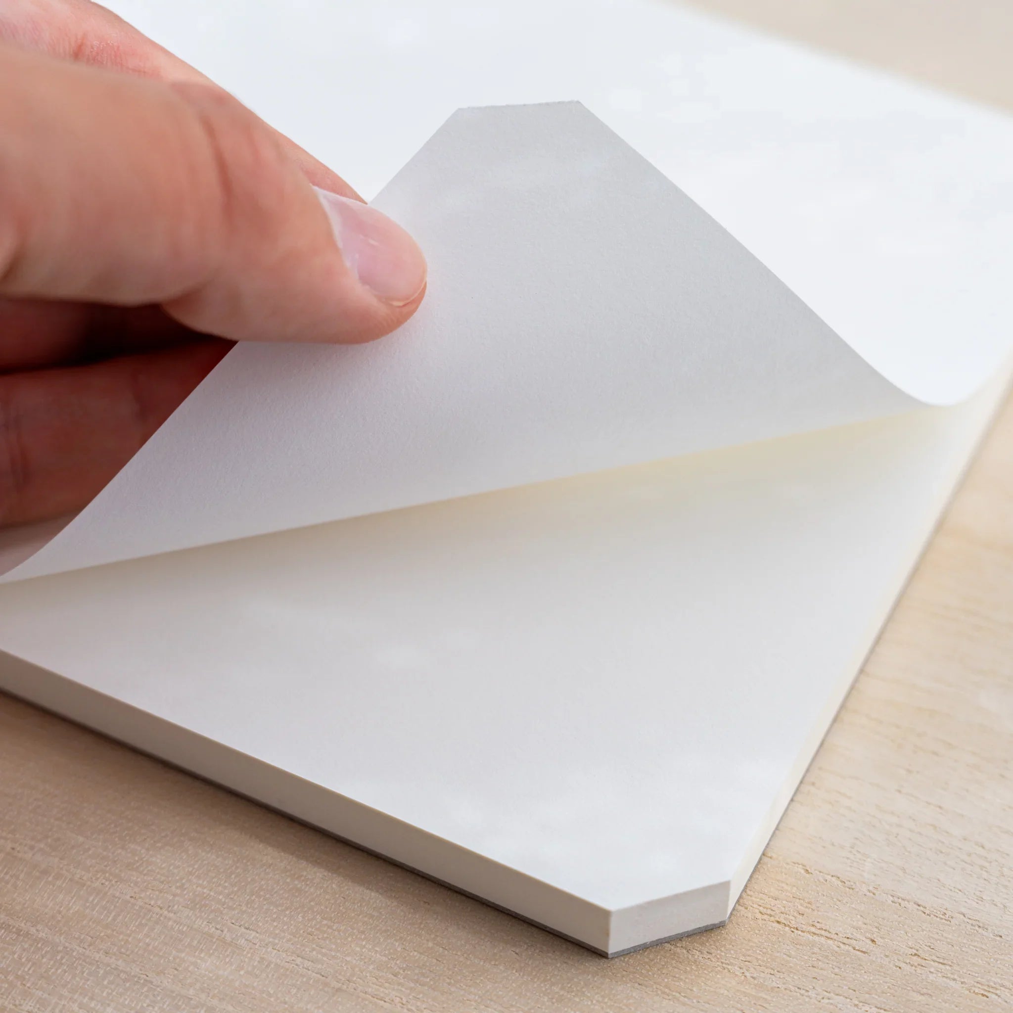 A hand lifting the blank white top sheet of a Midori MD Paper Pad Cotton A5, cut corner visible