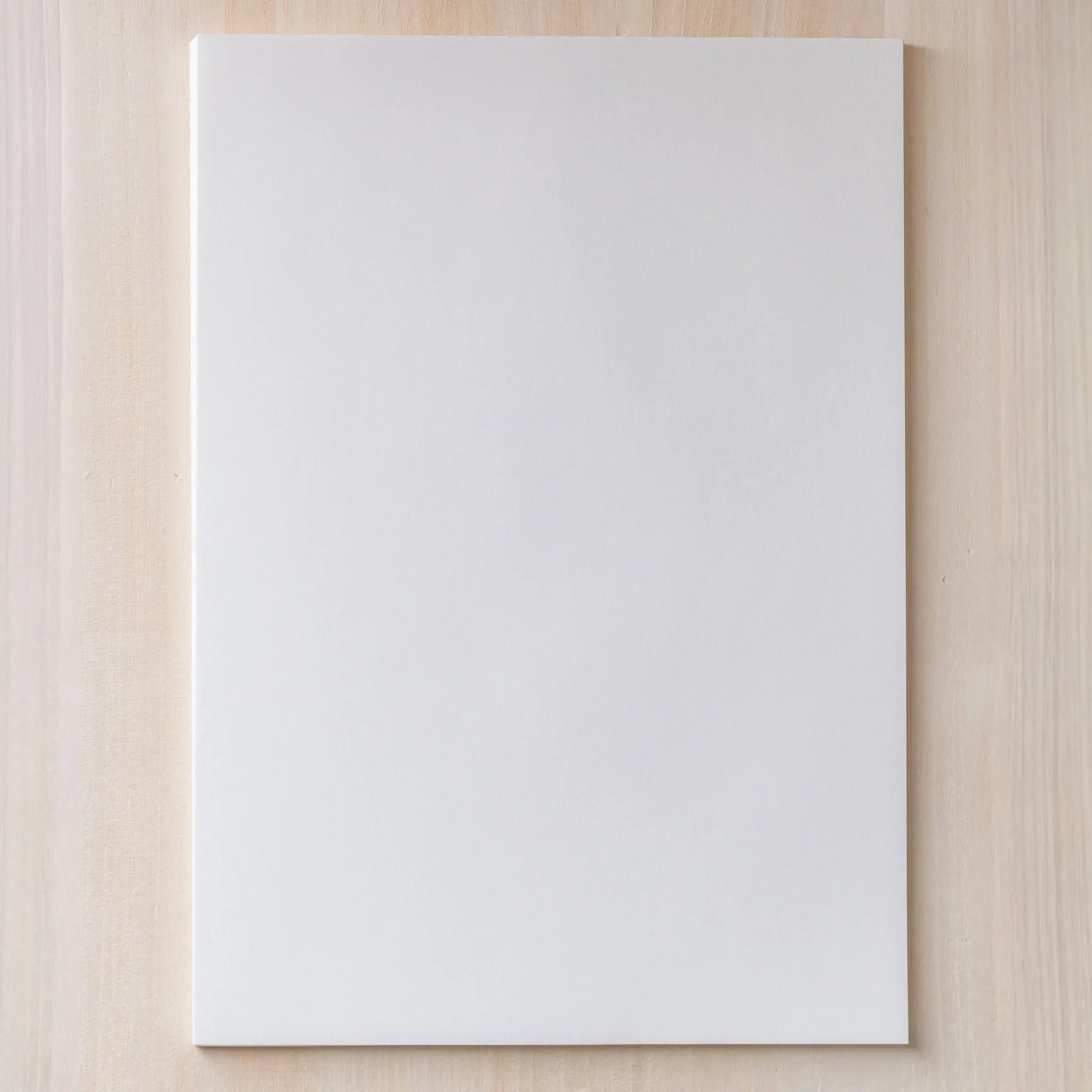 Single A4 sheet of Yamamoto Paper Meringue cream-tinted bulky book paper laid flat on a wood surface.
