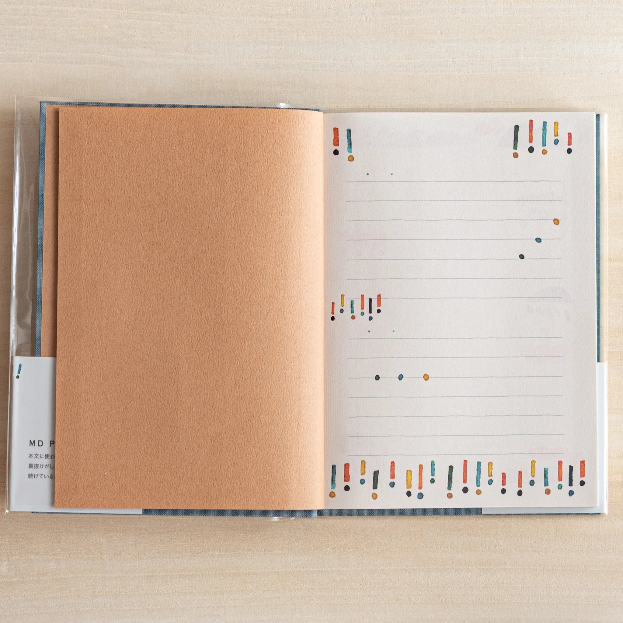 Open Midori Japanese journal showing lined page decorated with colorful exclamation marks and brown inside cover.