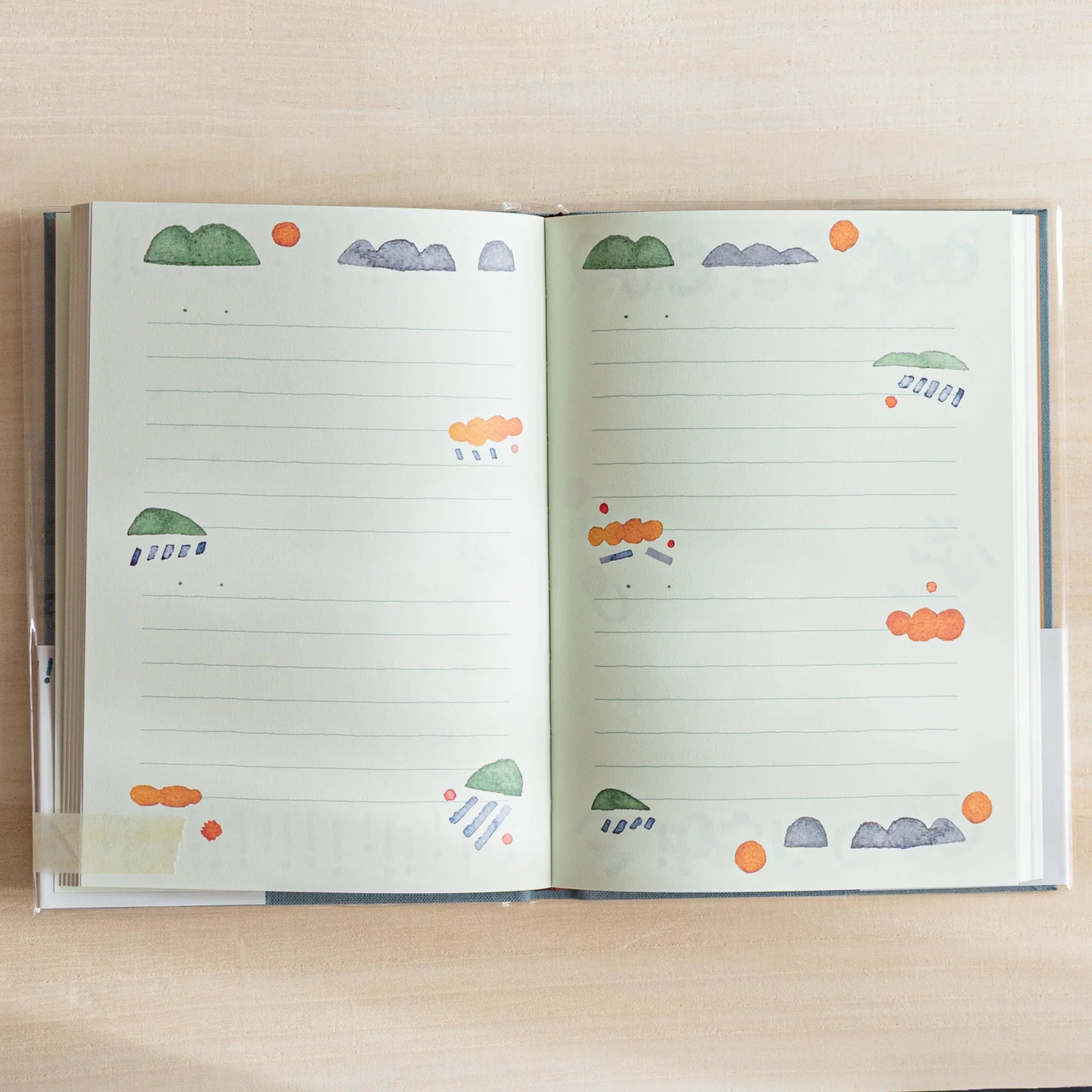 Open Midori Japanese journal showing lined pages with colorful cloud and hill motifs on light green background.