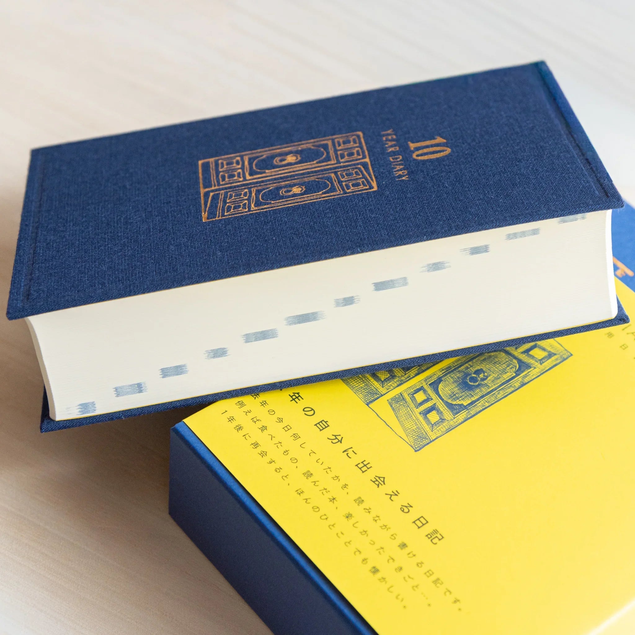 Midori Japanese journal 10-year diary gate design showing side view of navy book resting on yellow slipcase.