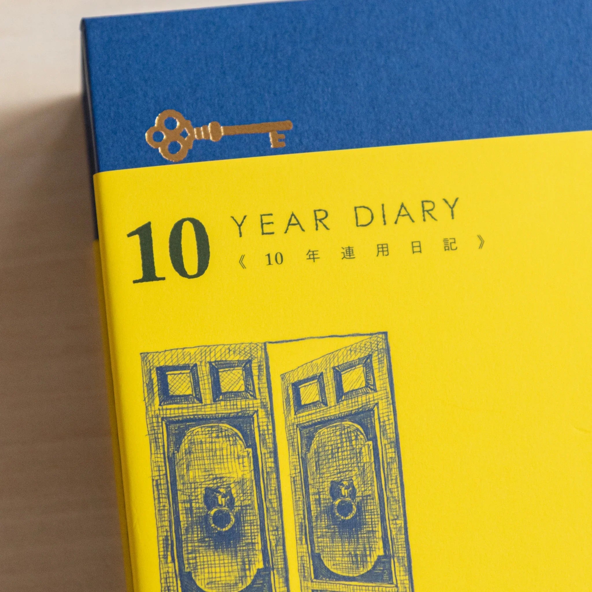Close-up of Midori Japanese journal 10-year diary gate design with navy top, golden key, and yellow cover door illustration.