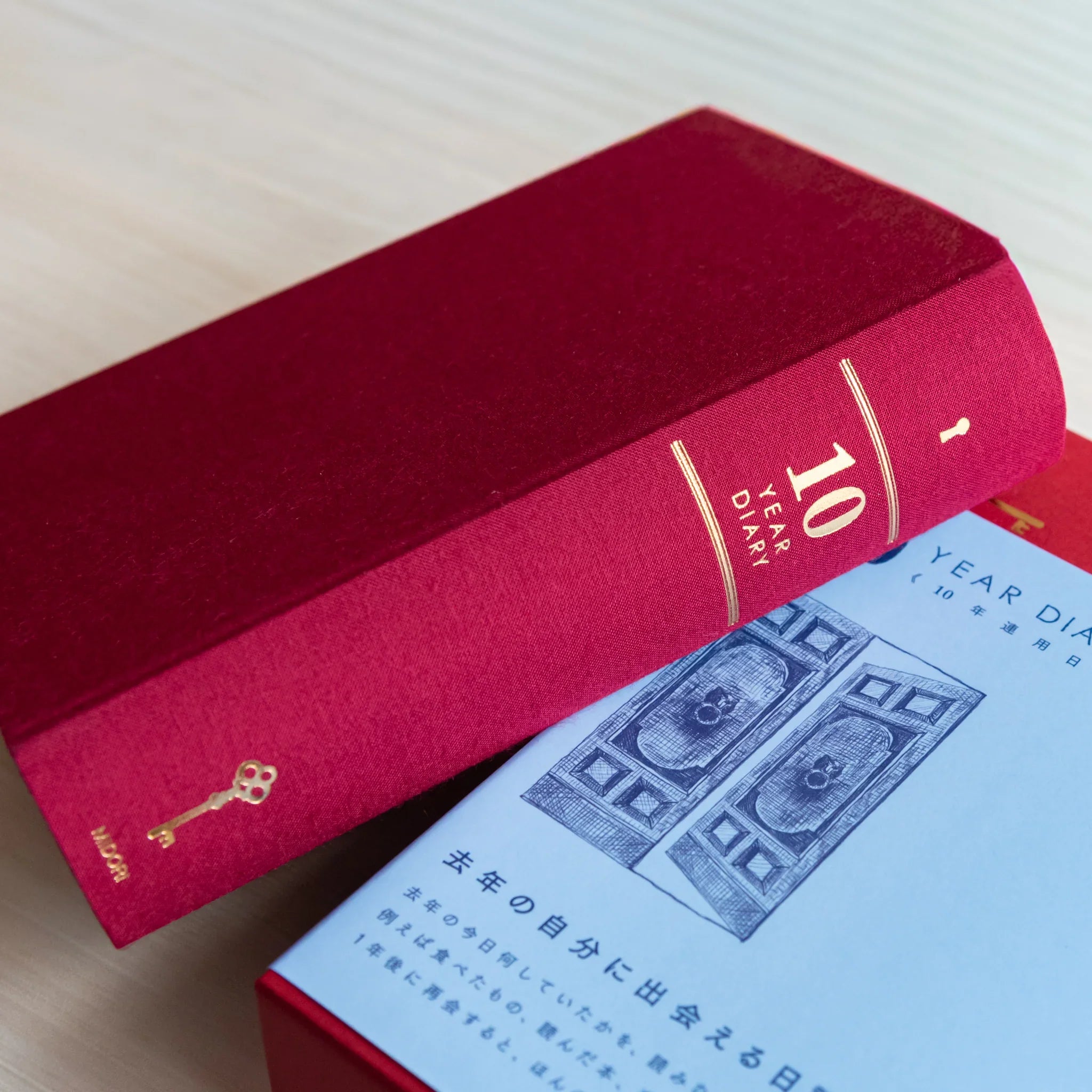 Midori Japanese journal 10-year diary gate design red book resting on blue slipcase with door illustration.