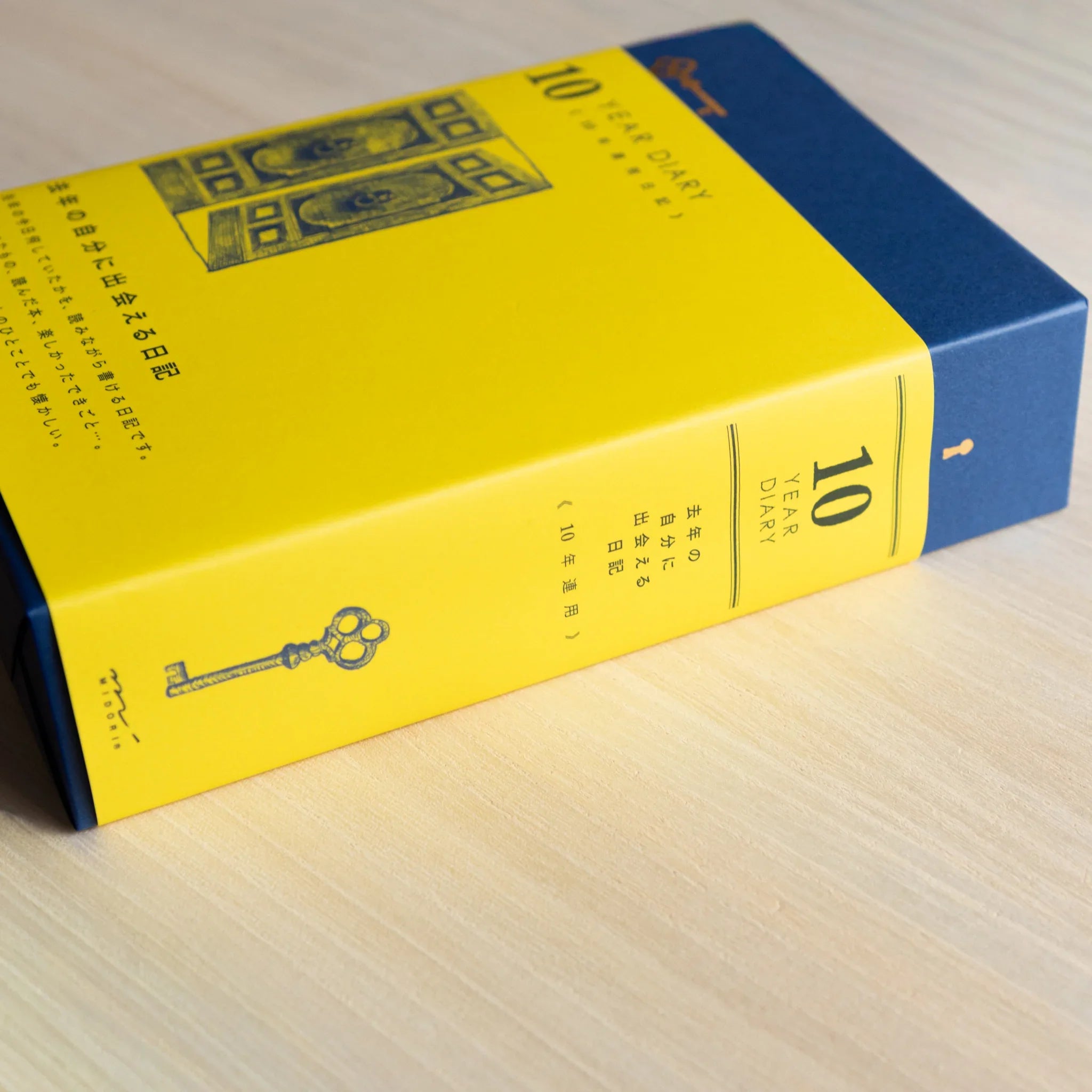 Side view of Midori Japanese journal 10-year diary gate design showing yellow spine with key illustration and navy top.