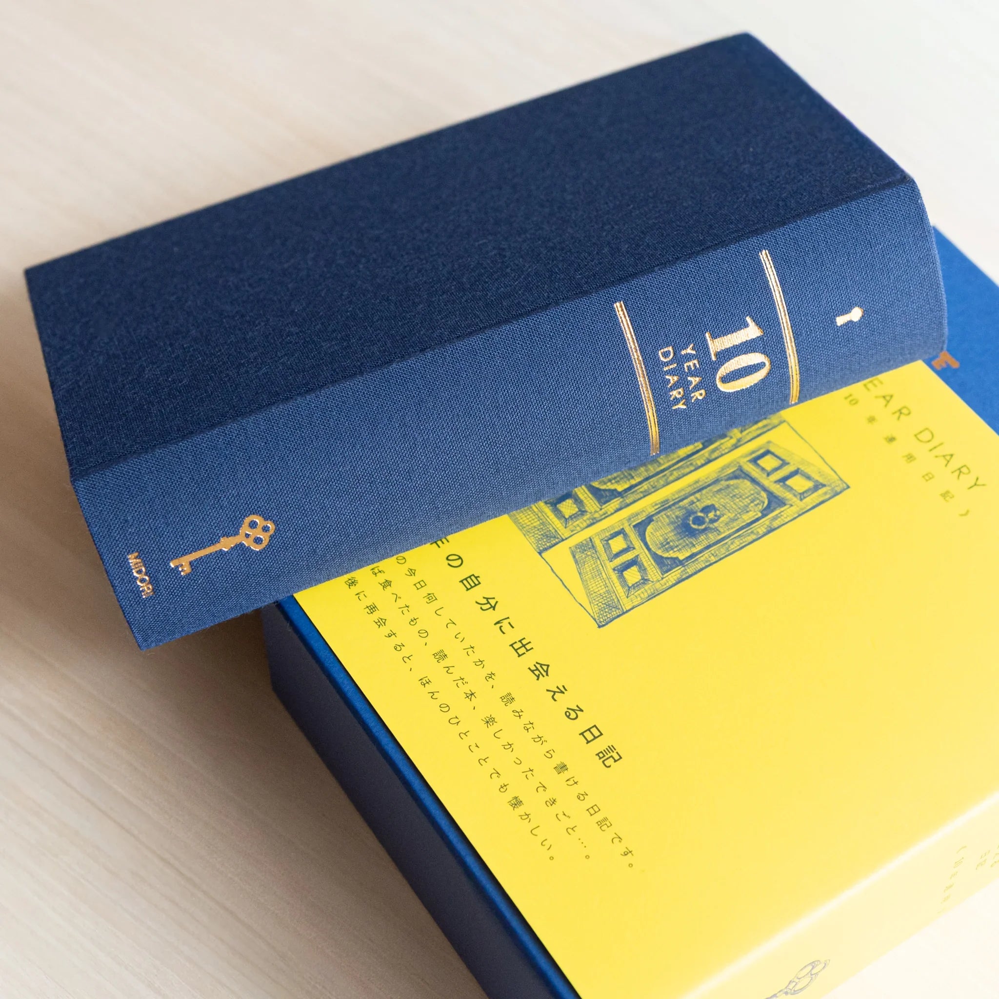 Midori Japanese journal 10-year diary gate design with navy book resting diagonally on yellow slipcase box.