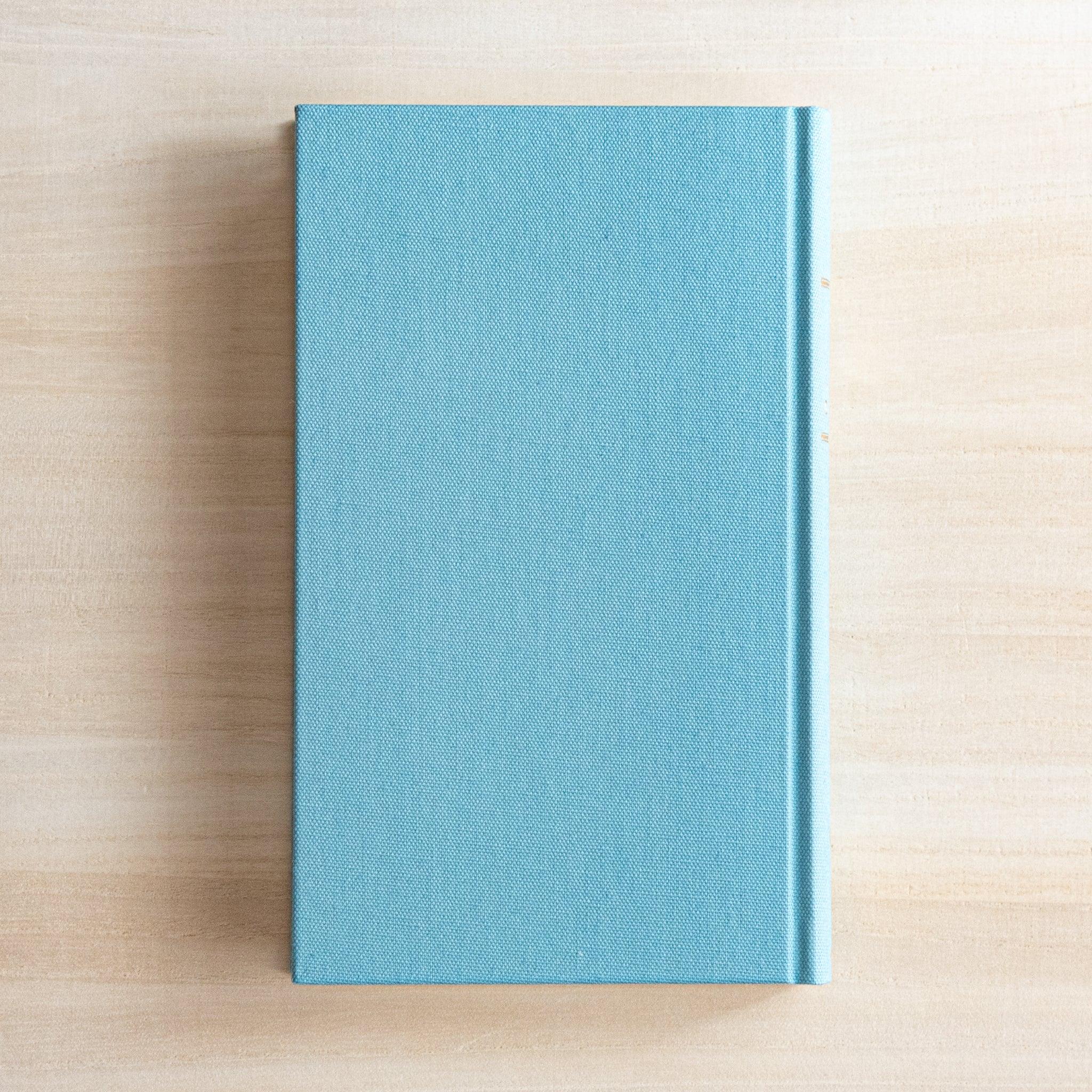 Back view of Midori Japanese journal 3 Year Diary Gate Design blue cloth hardcover on wooden surface.
