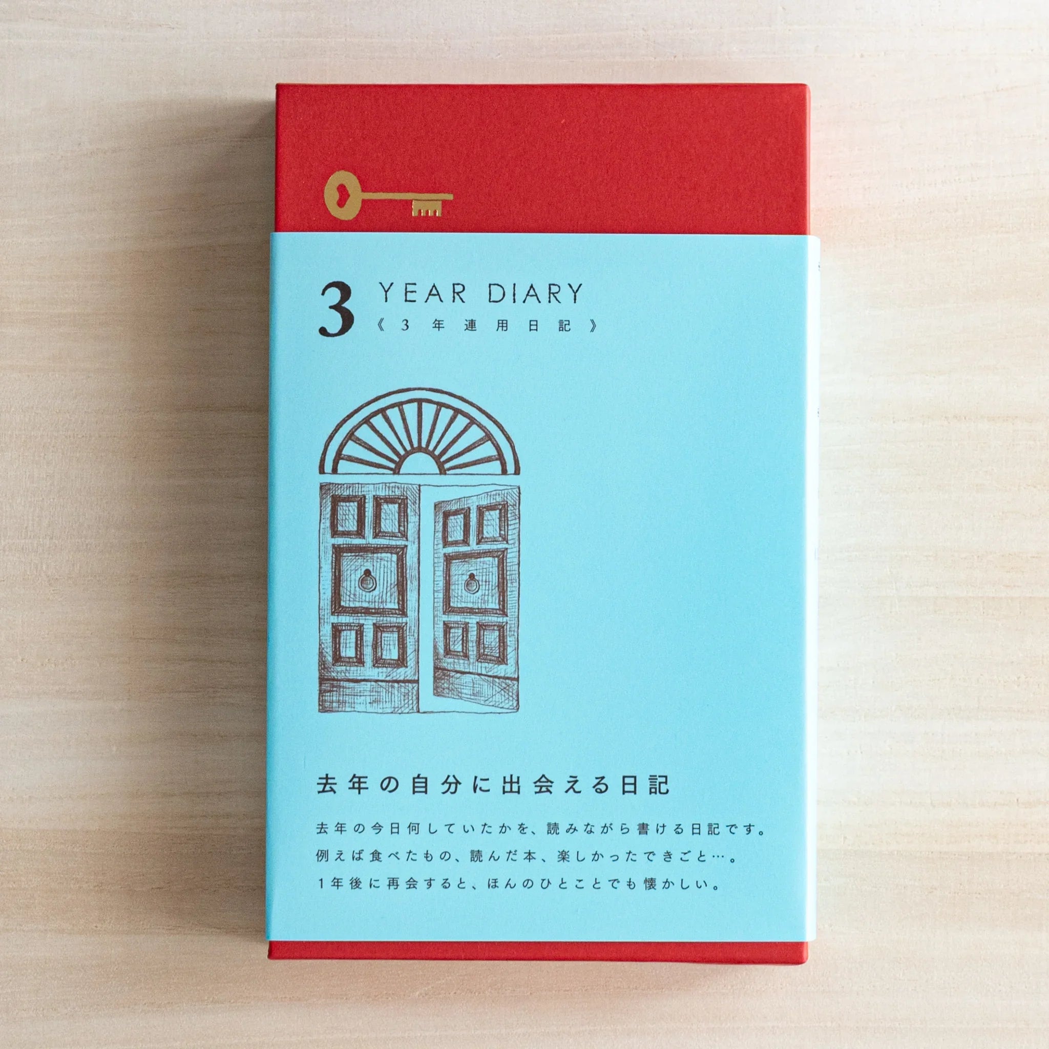 Front view of Midori Japanese journal 10‑year diary gate design in light blue box with red top and door illustration