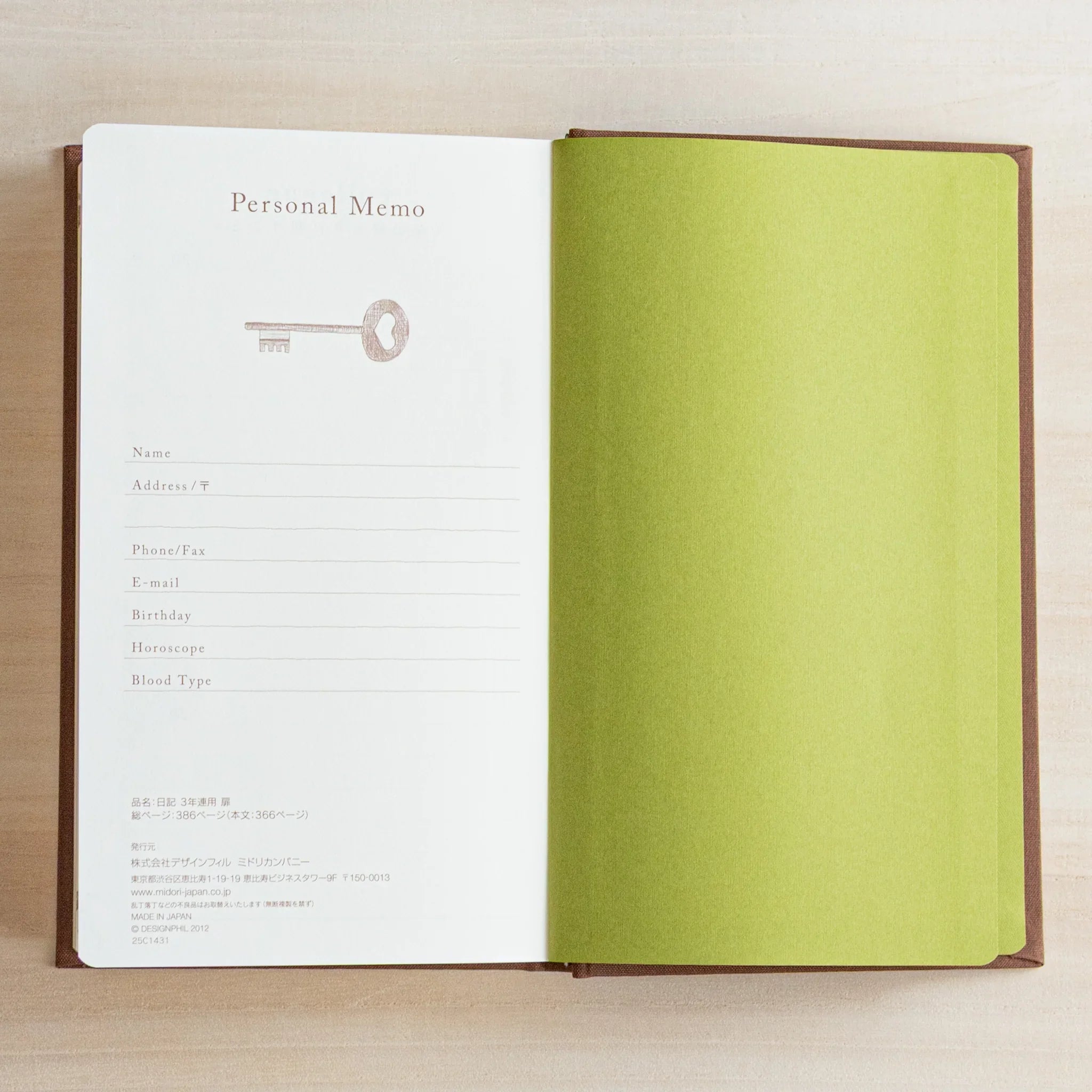 Open Midori Japanese Journal showing Personal Memo page with key illustration and green endpaper on wooden desk.