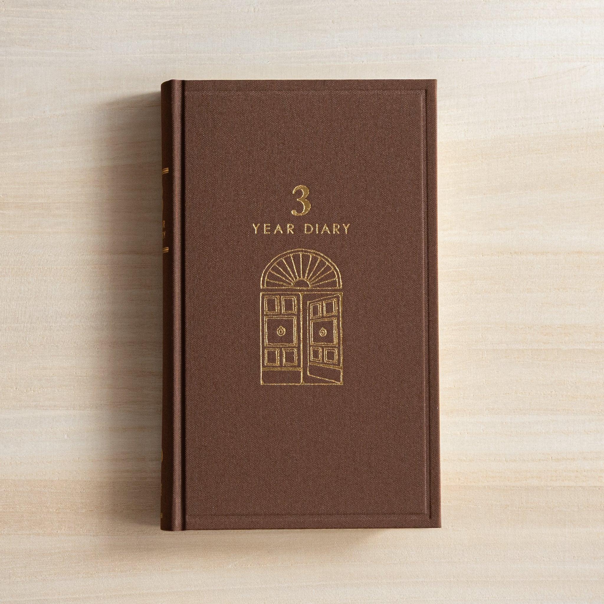 Front view of the brown Midori Japanese journal “3 Year Diary Gate Design” featuring a gold embossed door motif.