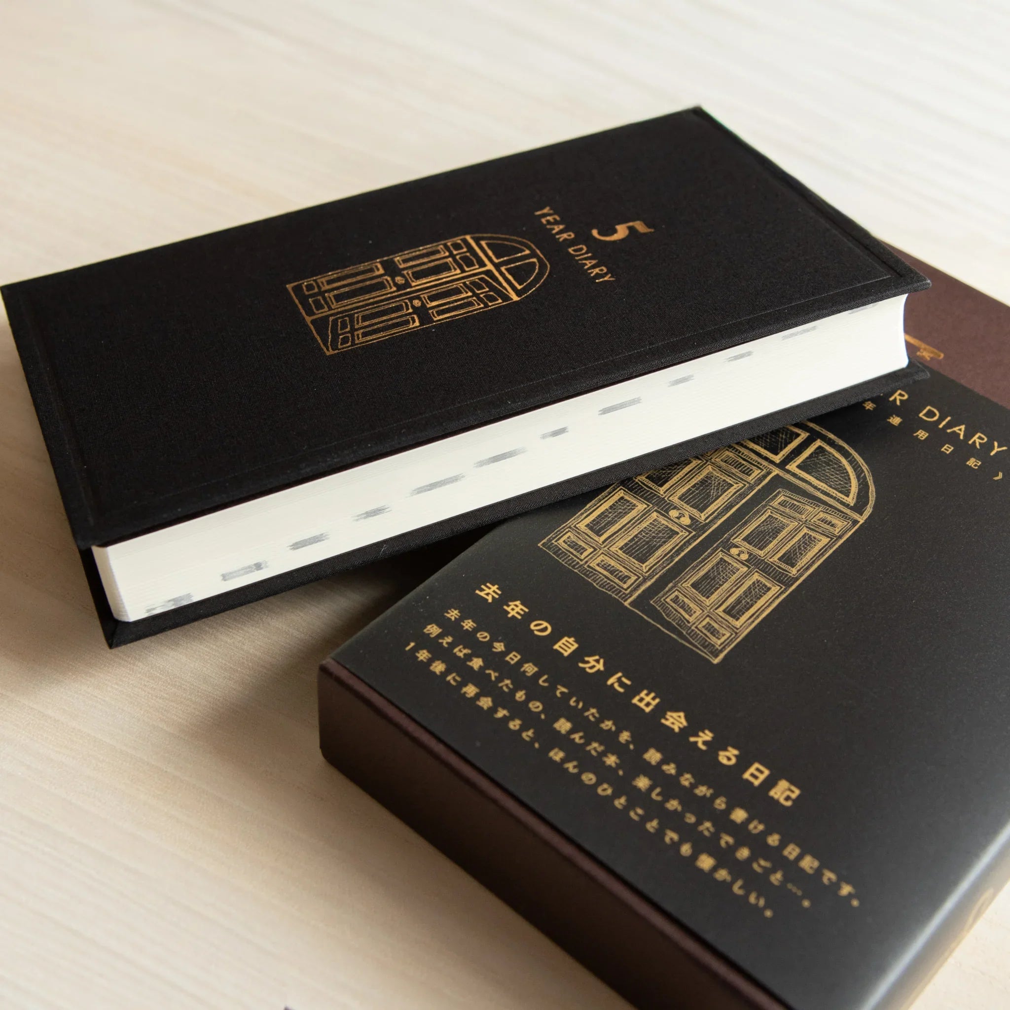 Midori 5 Year Journal Gate Design Japanese Journal partly out of black case angled view with gold bordered door on cover.