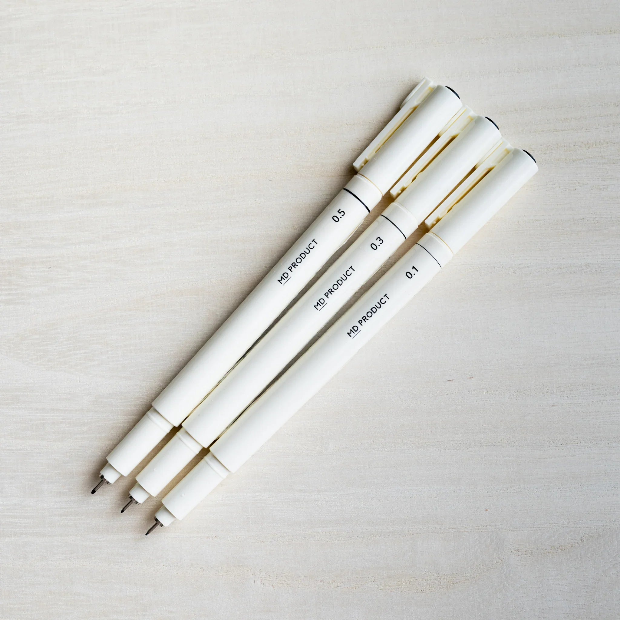Three Midori MD Drawing Pens lying diagonally with caps posted and fine tips exposed, marked 0.5, 0.3, and 0.1 mm