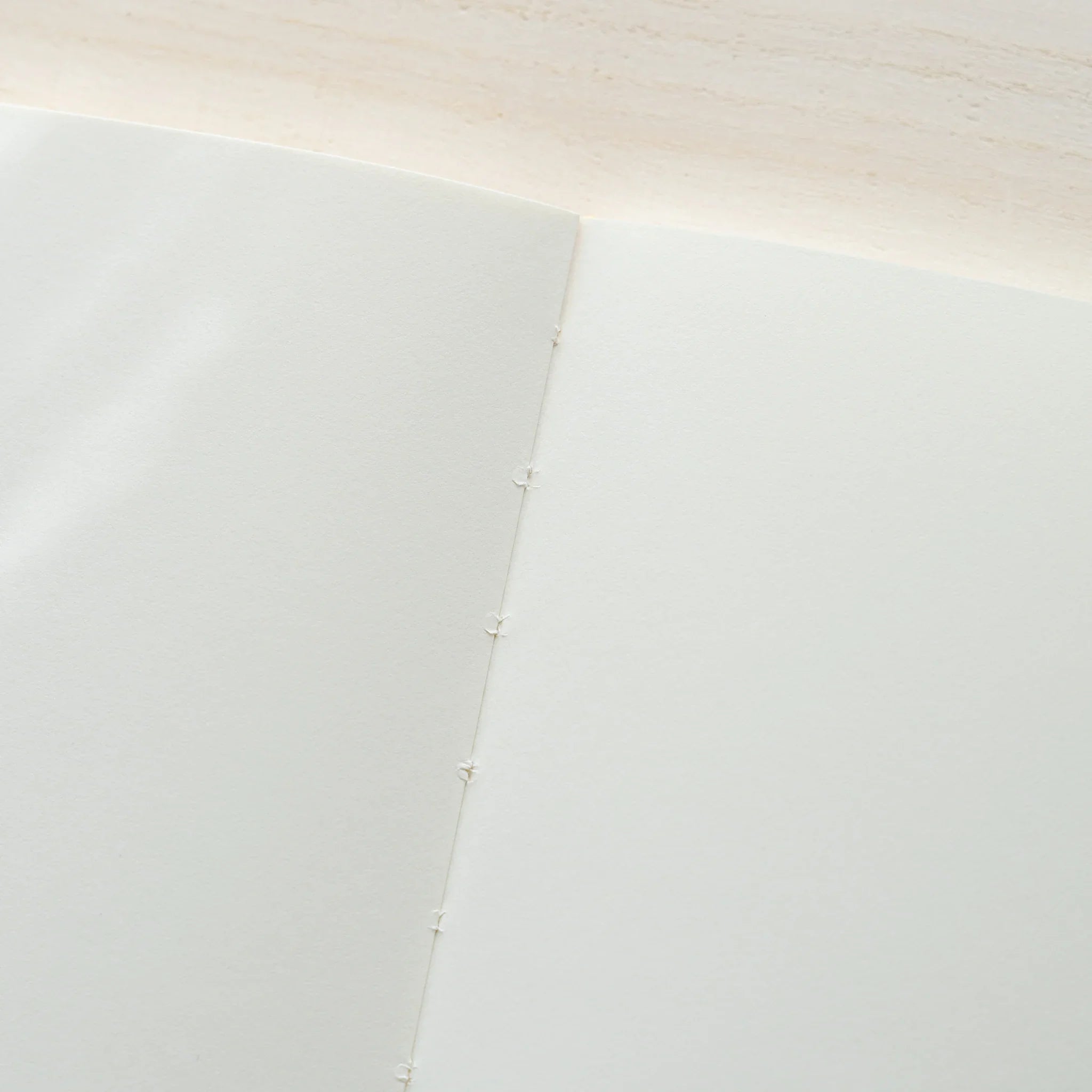 Midori MD Notebook A5 opened to blank ivory pages, close-up showing thread-stitching detail on center spine