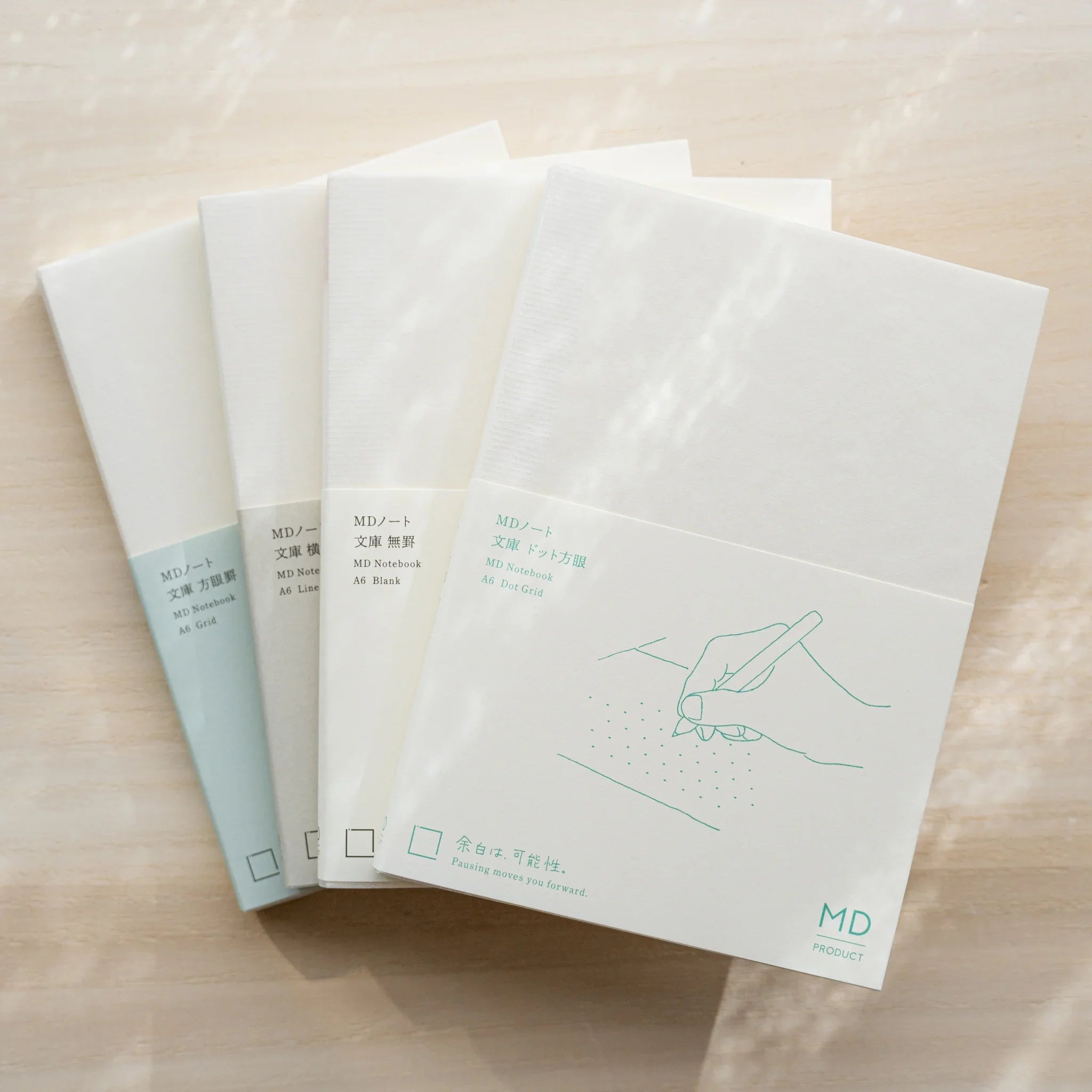 Four Midori MD Notebook A6 variants fanned out with glassine covers, showing Dot Grid, Blank, Lined, and Grid editions