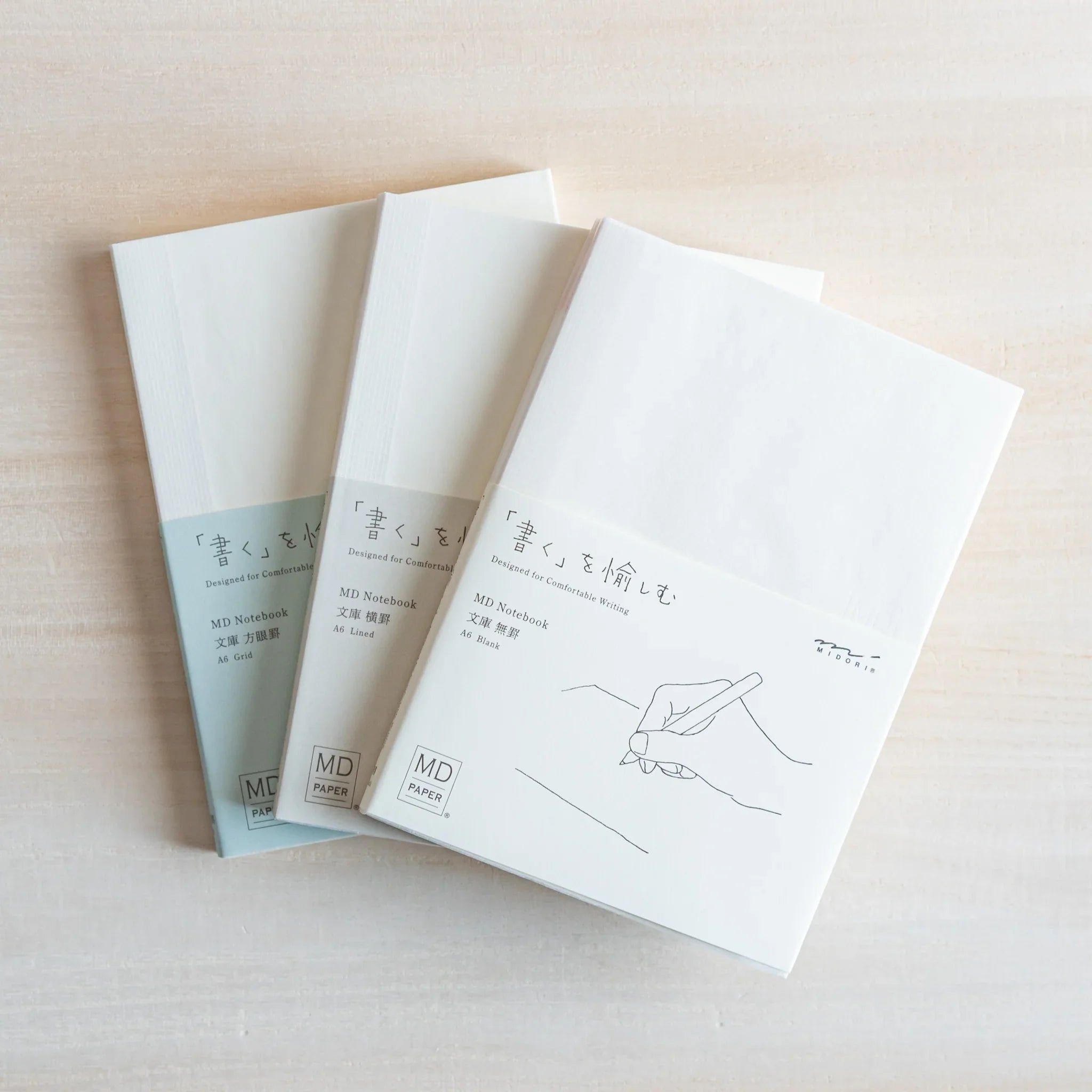 Japanese Notebook Midori MD A6 notebooks stacked on a light wooden surface, featuring clean white covers.