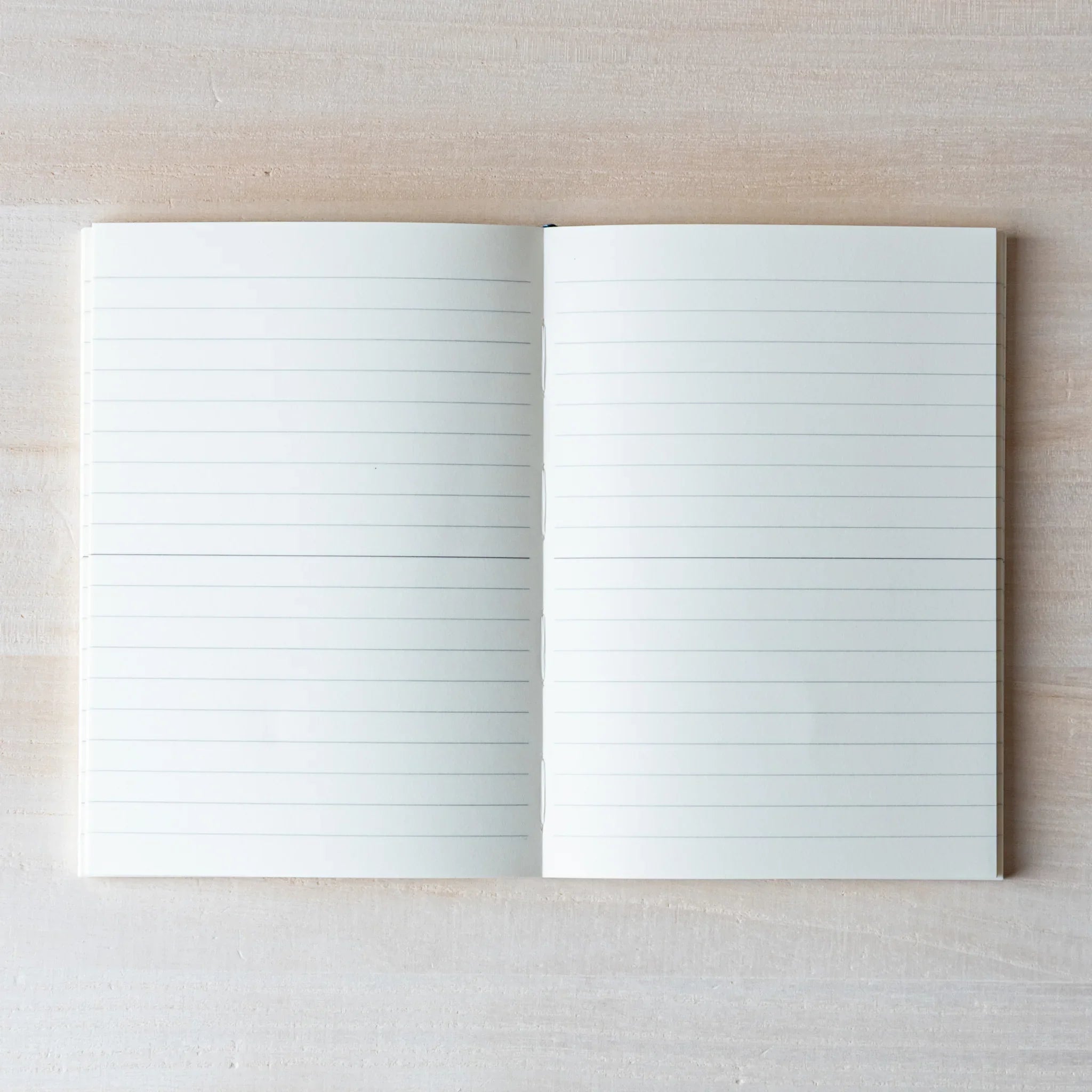 Japanese Notebook Midori MD A6 opened flat, showing lined pages on a light wooden surface.