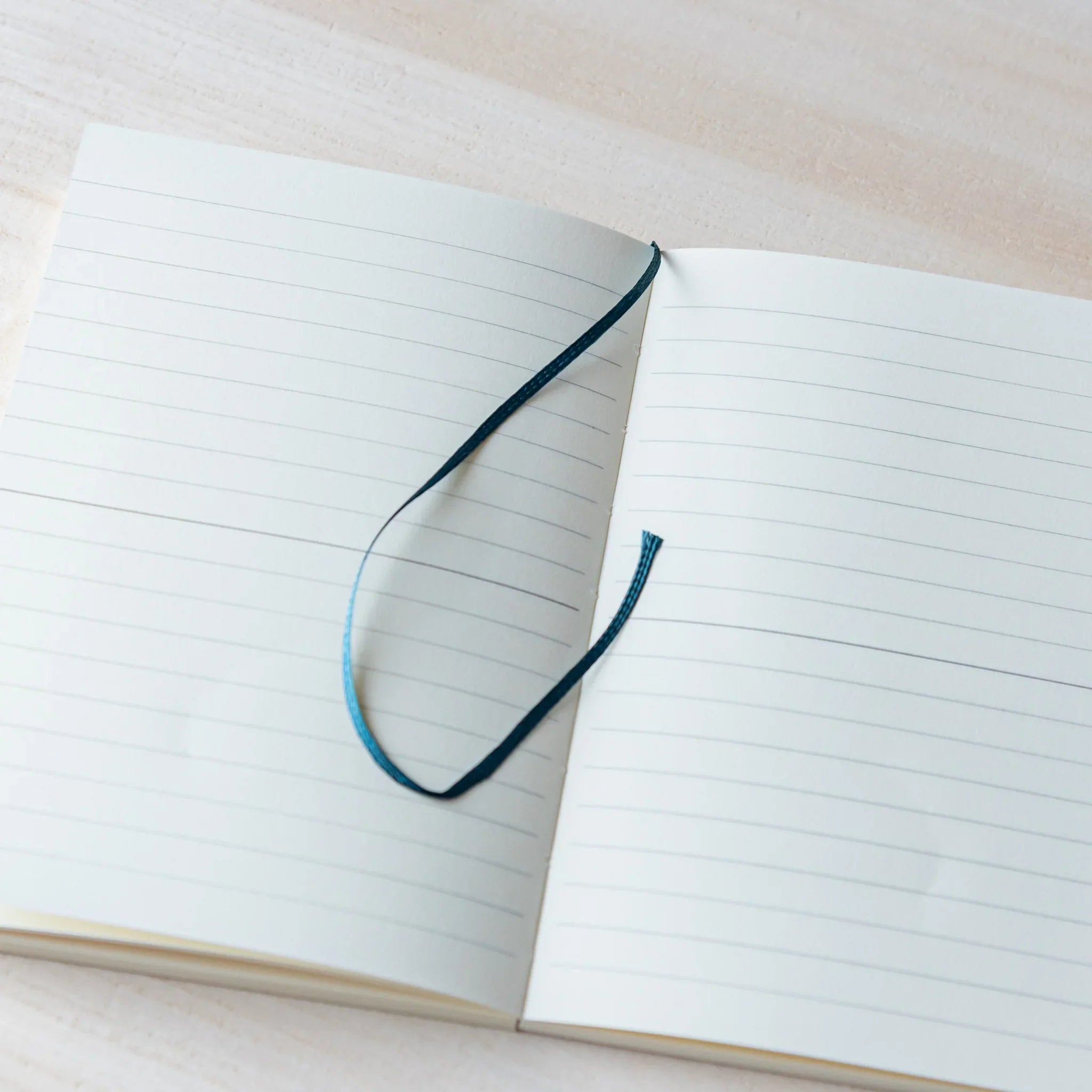 Japanese Notebook Midori MD A6 opened flat, showing lined pages with a ribbon bookmark.