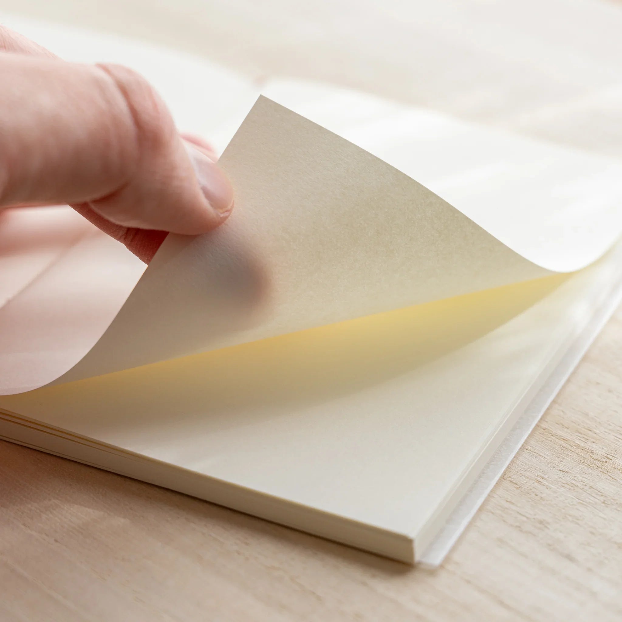 Hand turning a page of Midori MD Notebook A6 Blank, ivory pages visible, rounded corners, notebook on wooden surface