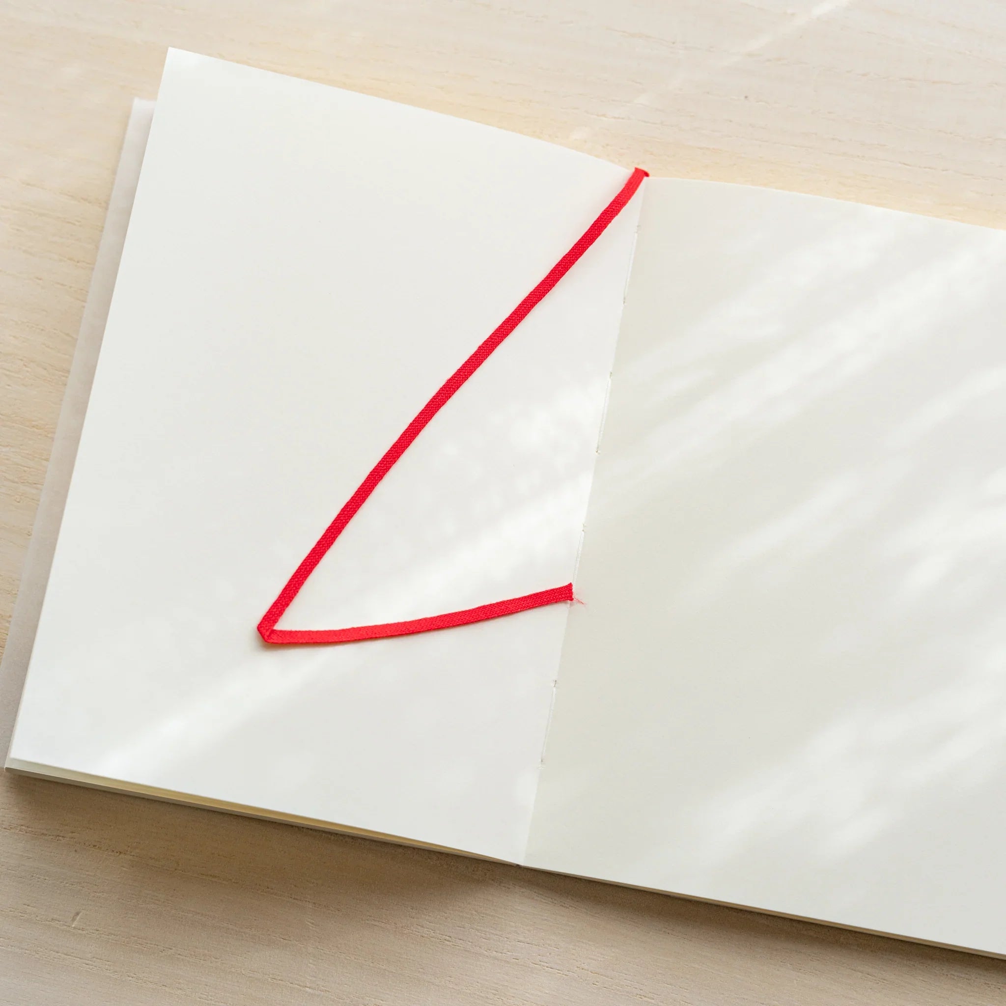 Midori MD Notebook A6 Blank open flat from above, blank ivory pages with red bookmark ribbon lying diagonally across spread