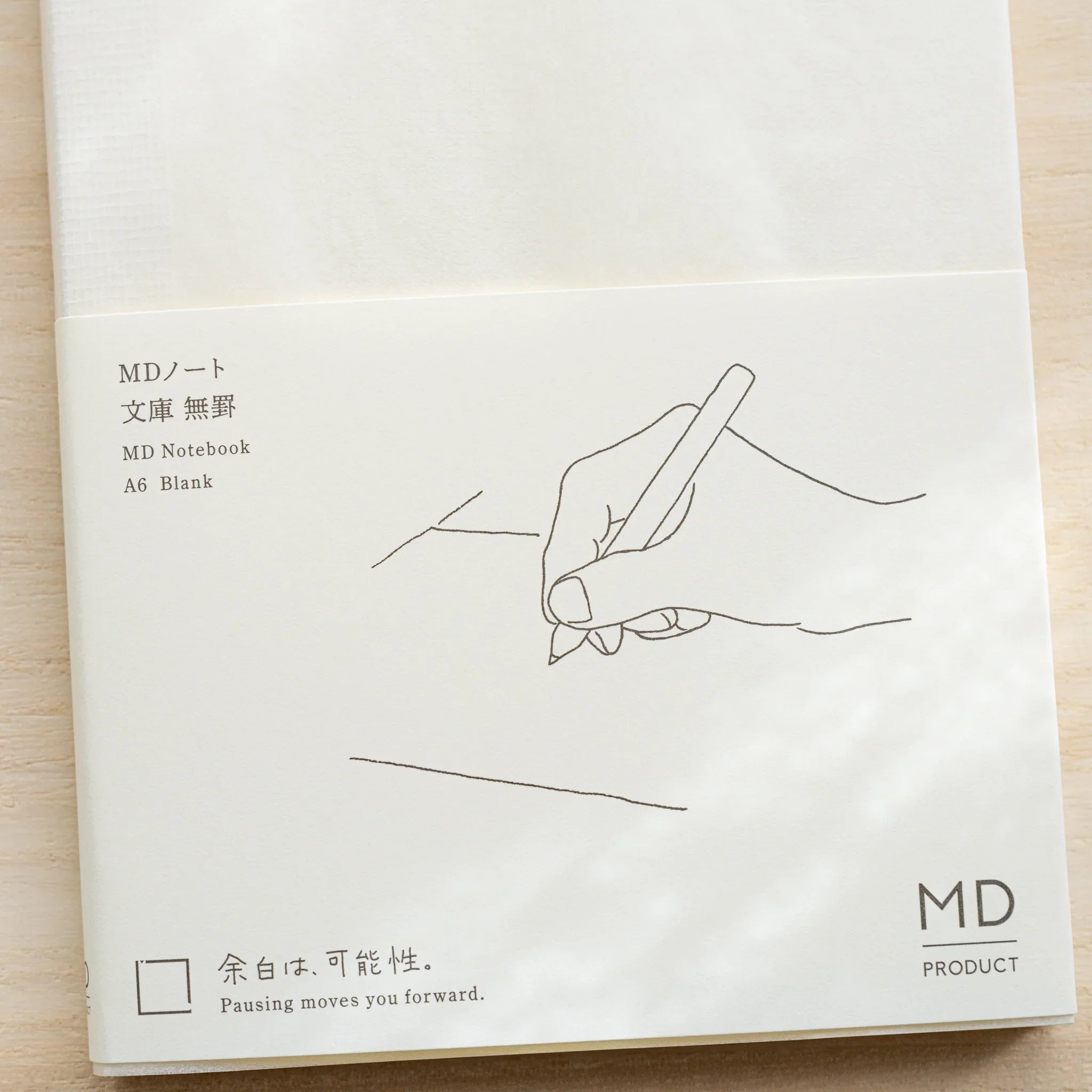 Midori MD Notebook A6 Blank glassine cover laid flat showing black hand-writing illustration, product name, and MD Product logo