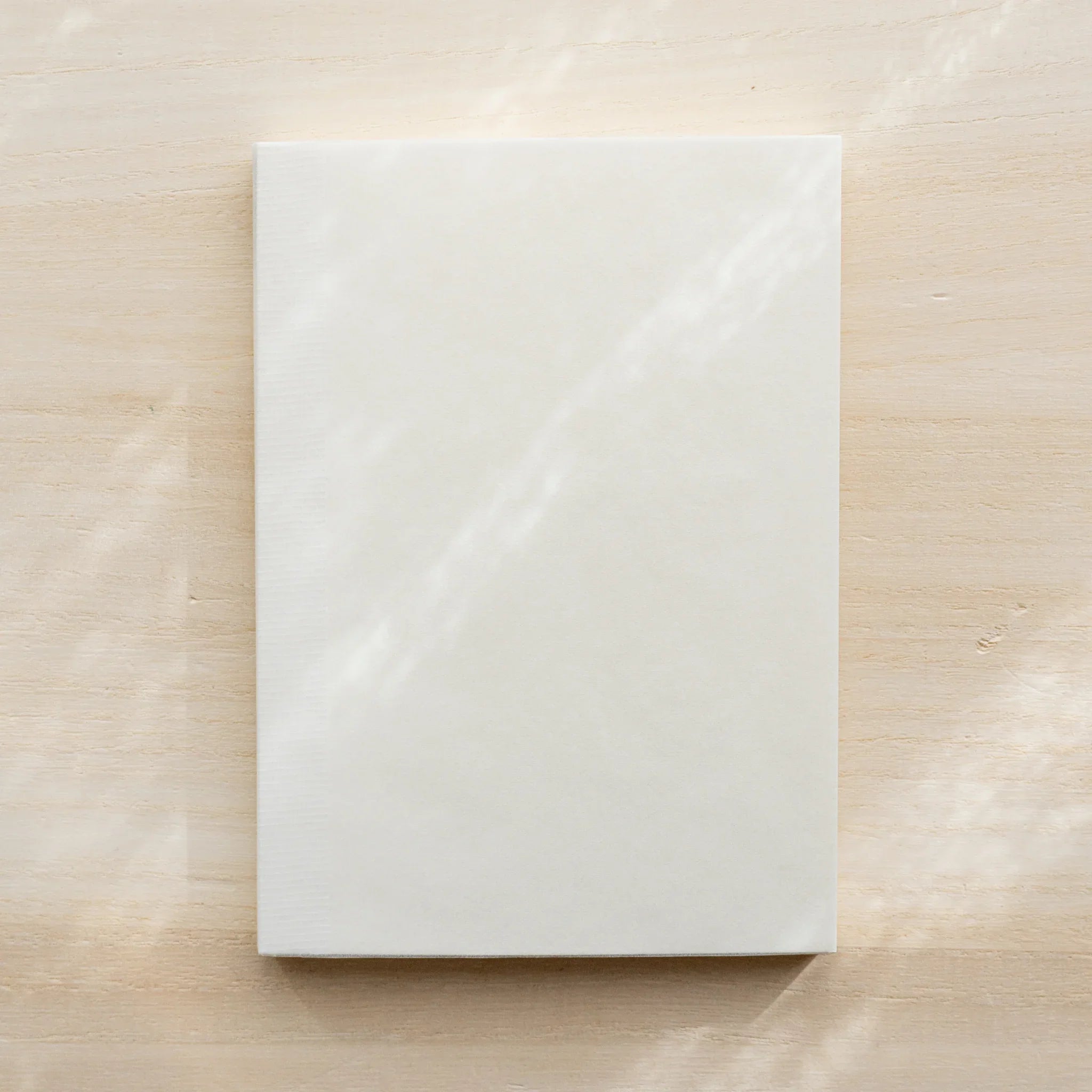 Midori MD Notebook A6 Grid closed, plain white glassine outer cover, no belly band, on wooden surface