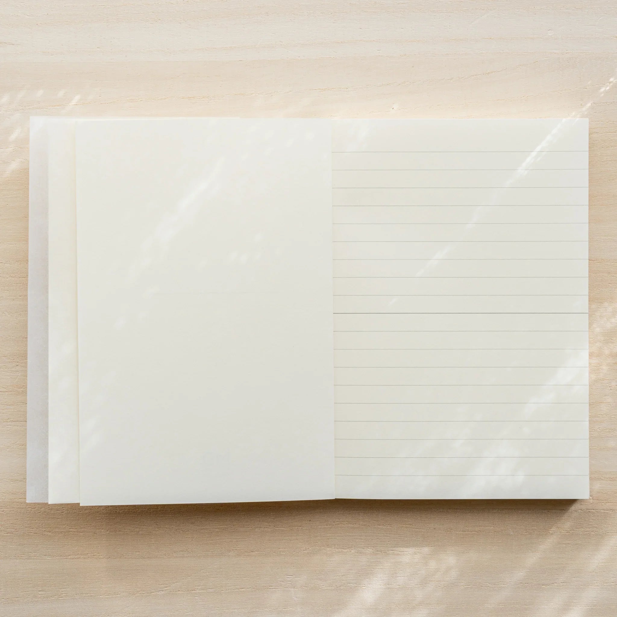 Midori MD Notebook A6 Lined open flat from above, glassine inner cover on left, ivory lined page on right with center spine