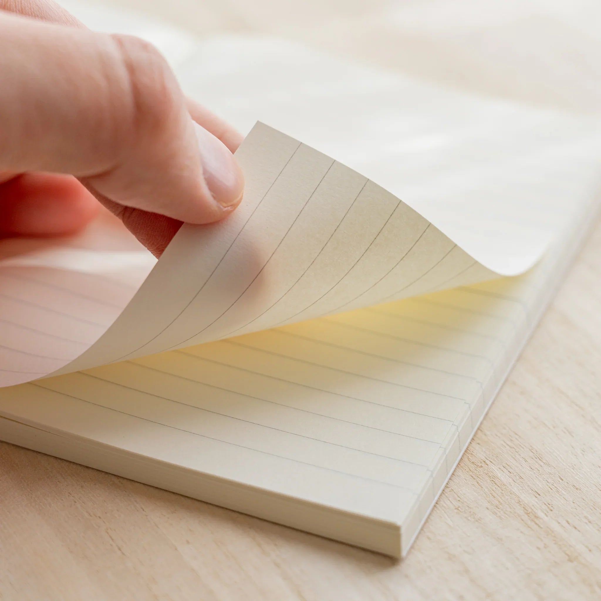Hand turning a page of Midori MD Notebook A6 Lined, ivory lined pages visible, rounded corners, notebook on wooden surface