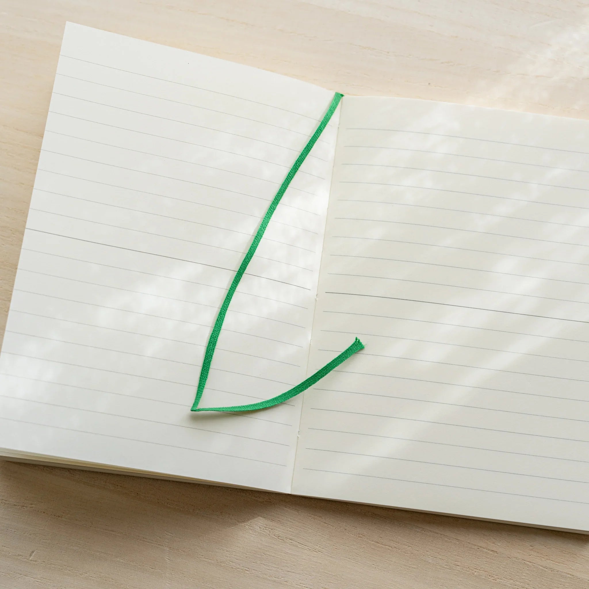 Midori MD Notebook A6 Lined open flat from above, ivory lined pages with green bookmark ribbon lying diagonally across spread