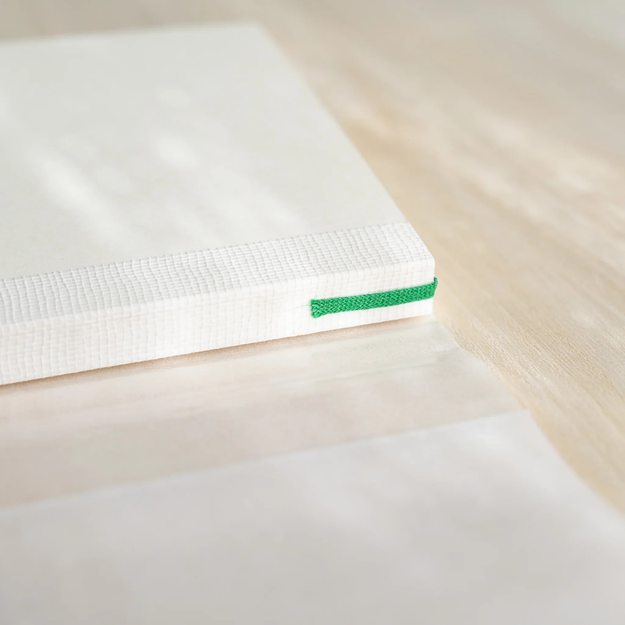 Midori MD Notebook A6 Lined spine close-up showing white thread-stitched binding with green bookmark ribbon at bottom edge