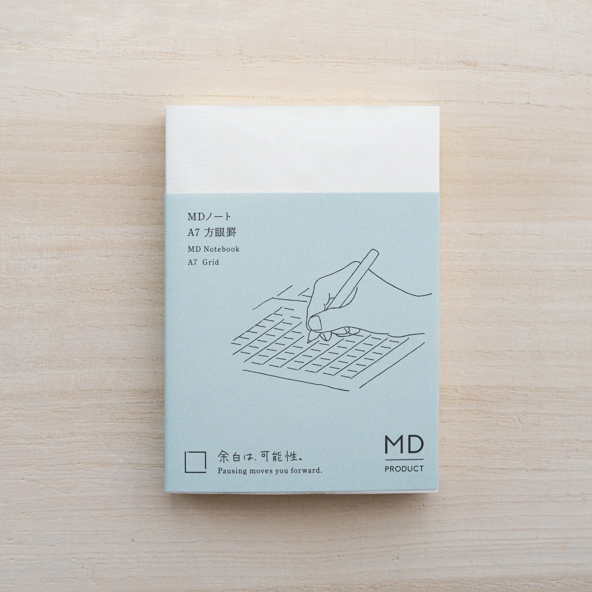MD Notebook A7 in cream cover with paper belly band showing a hand-with-pen line drawing