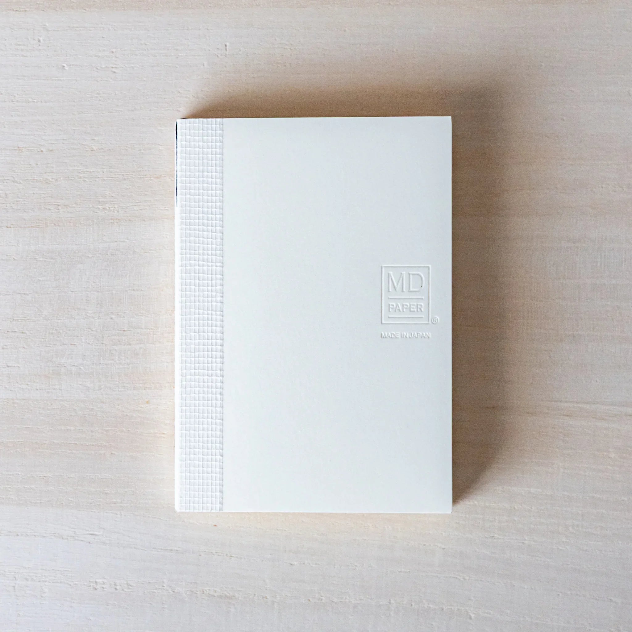 Japanese Notebook top-down view of a closed Midori MD A7 notebook with a white cover and exposed spine on a table.