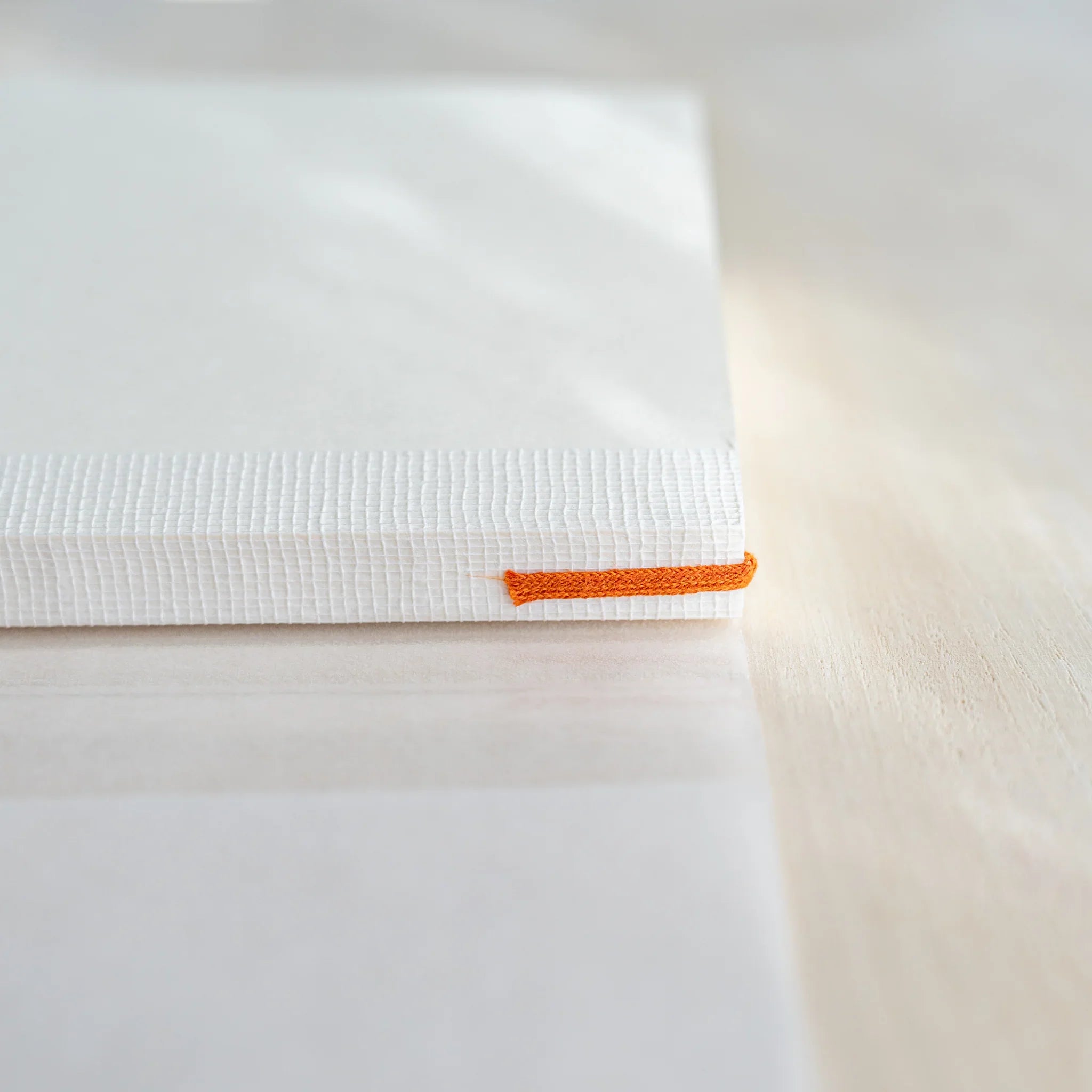 Close-up of Midori MD Notebook B6 Slim spine, white cloth binding, orange ribbon bookmark visible, ivory page edges