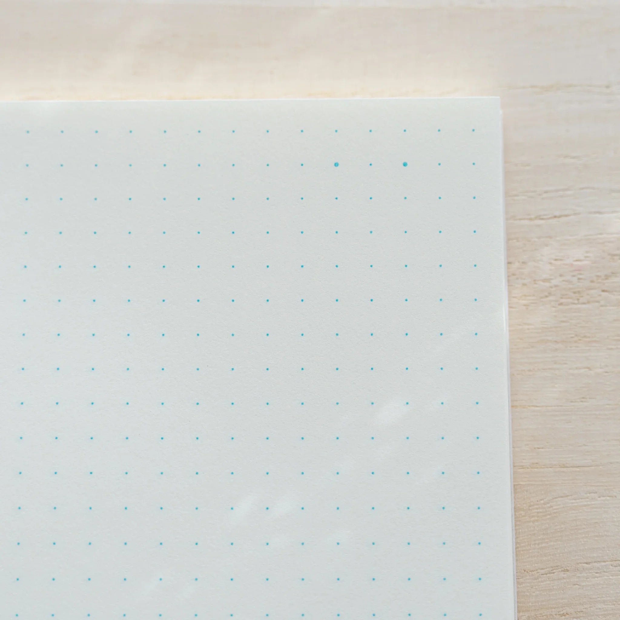 Close-up of single Midori MD Notebook B6 Slim dot grid page showing teal blue dots on ivory paper, wood surface at edge