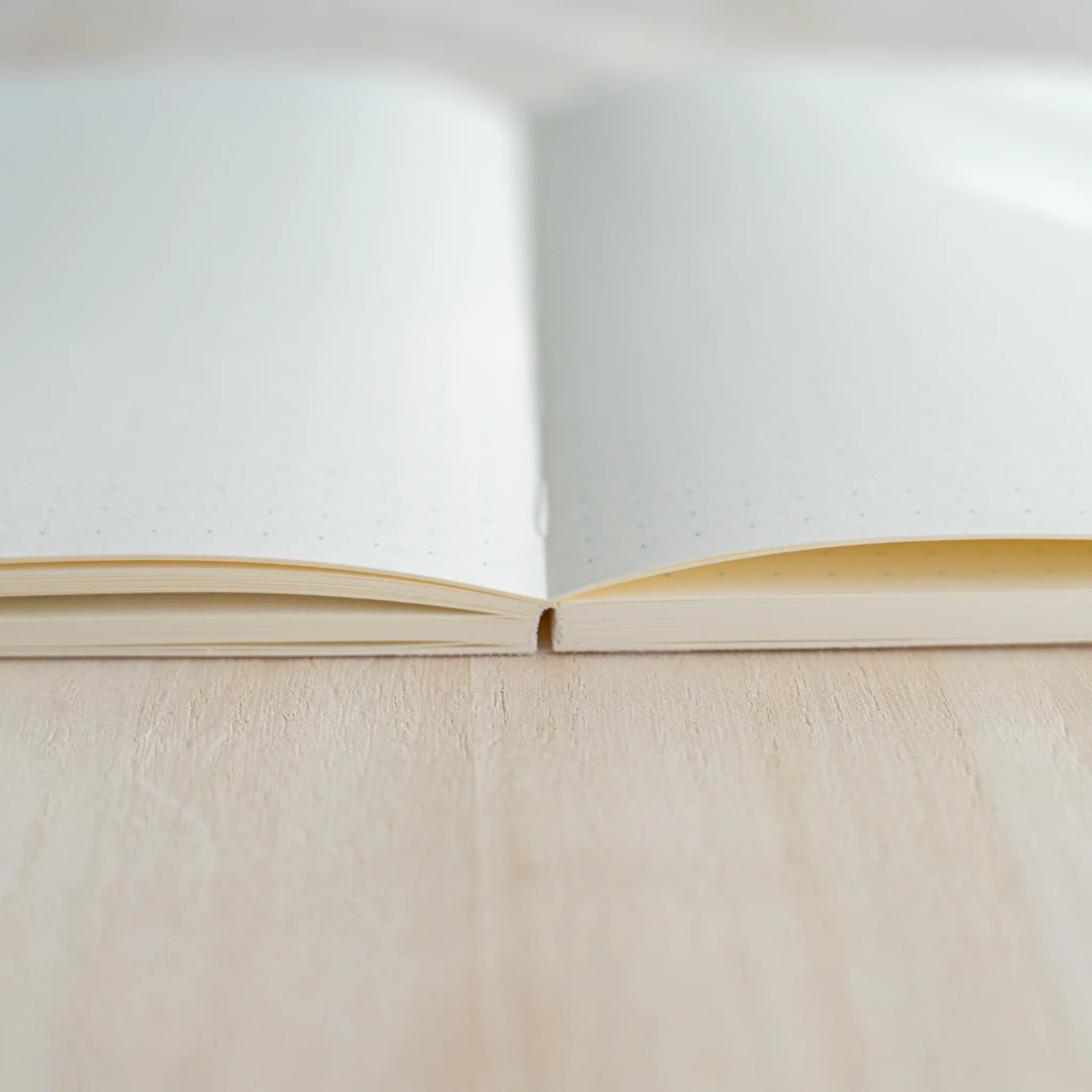 Side view of Midori MD Notebook B6 Slim open flat, showing cream ivory pages and thread-stitched spine on light wood