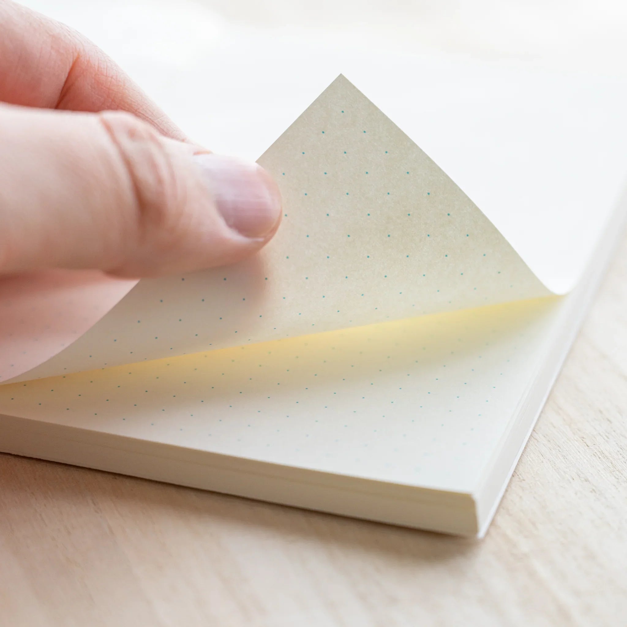 Hand turning a page of Midori MD Notebook B6 Slim showing ivory dot grid paper thickness and rounded corner
