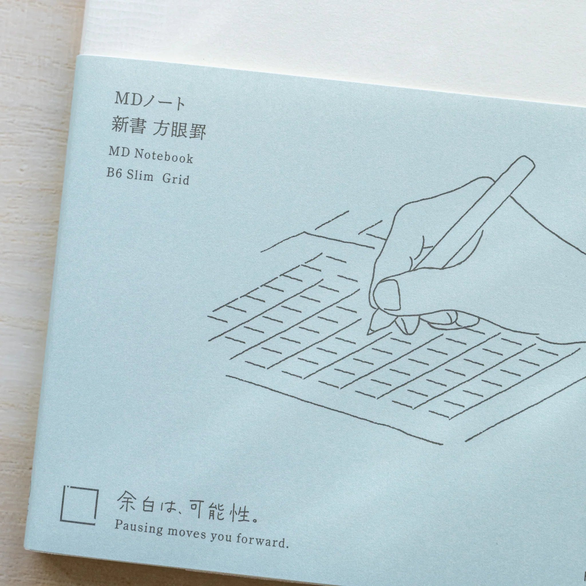 Close-up of Midori MD Notebook B6 Slim Grid teal cover with hand on grid illustration, Japanese and English text labels
